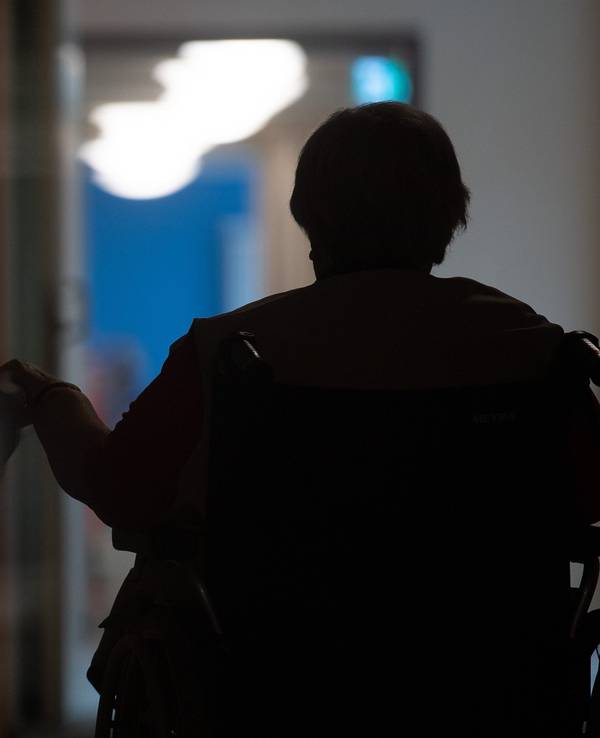 Eine Frau sitzt in einem Alten- und Pflegeheim in einem Rollstuhl auf einem Gang.