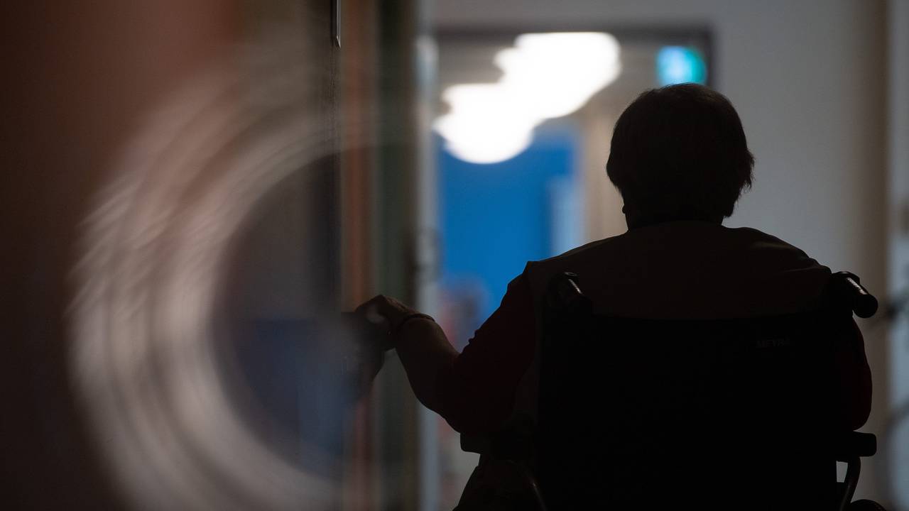 Eine Frau sitzt in einem Alten- und Pflegeheim in einem Rollstuhl auf einem Gang.