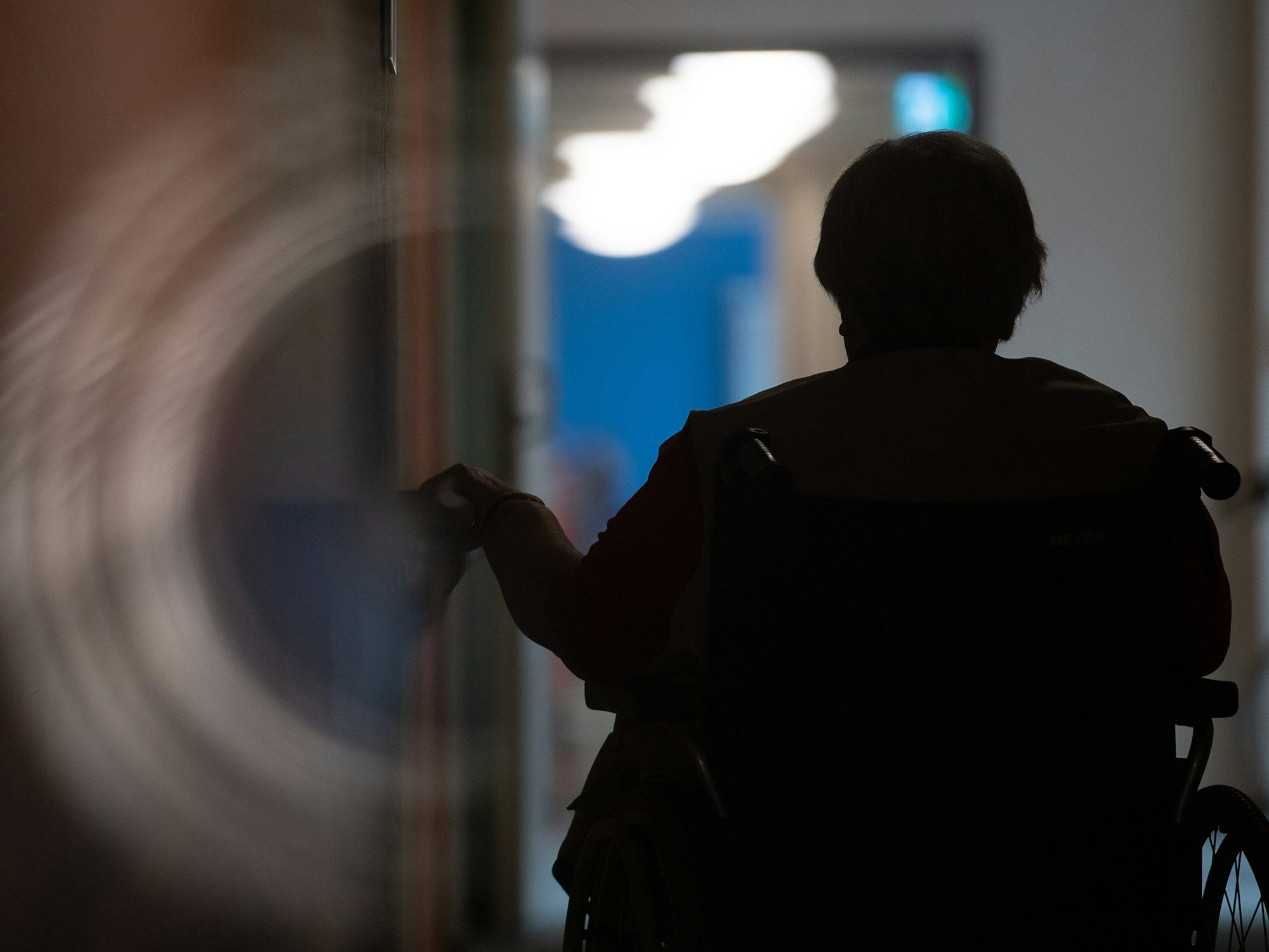 Eine Frau sitzt in einem Alten- und Pflegeheim in einem Rollstuhl auf einem Gang.