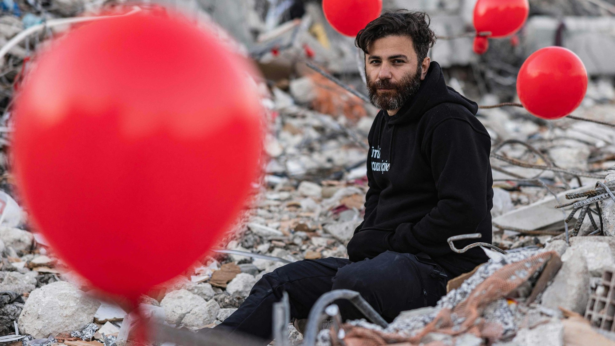 Ogun Sever Okur, ein 38-jähriger Türke, zwischen Luftballons, die an den Trümmern eines eingestürzten Gebäudes in Antakya in der Südtürkei hängen. Vielen Menschen im Erdbebengebiet droht nun die nächste Katastrophe.