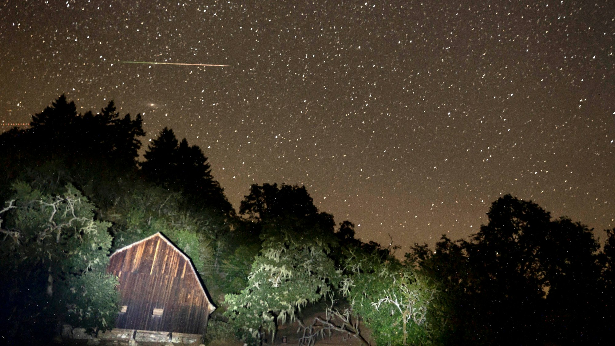 Ein Meteor zieht am Himmel über einer Scheune vorbei.