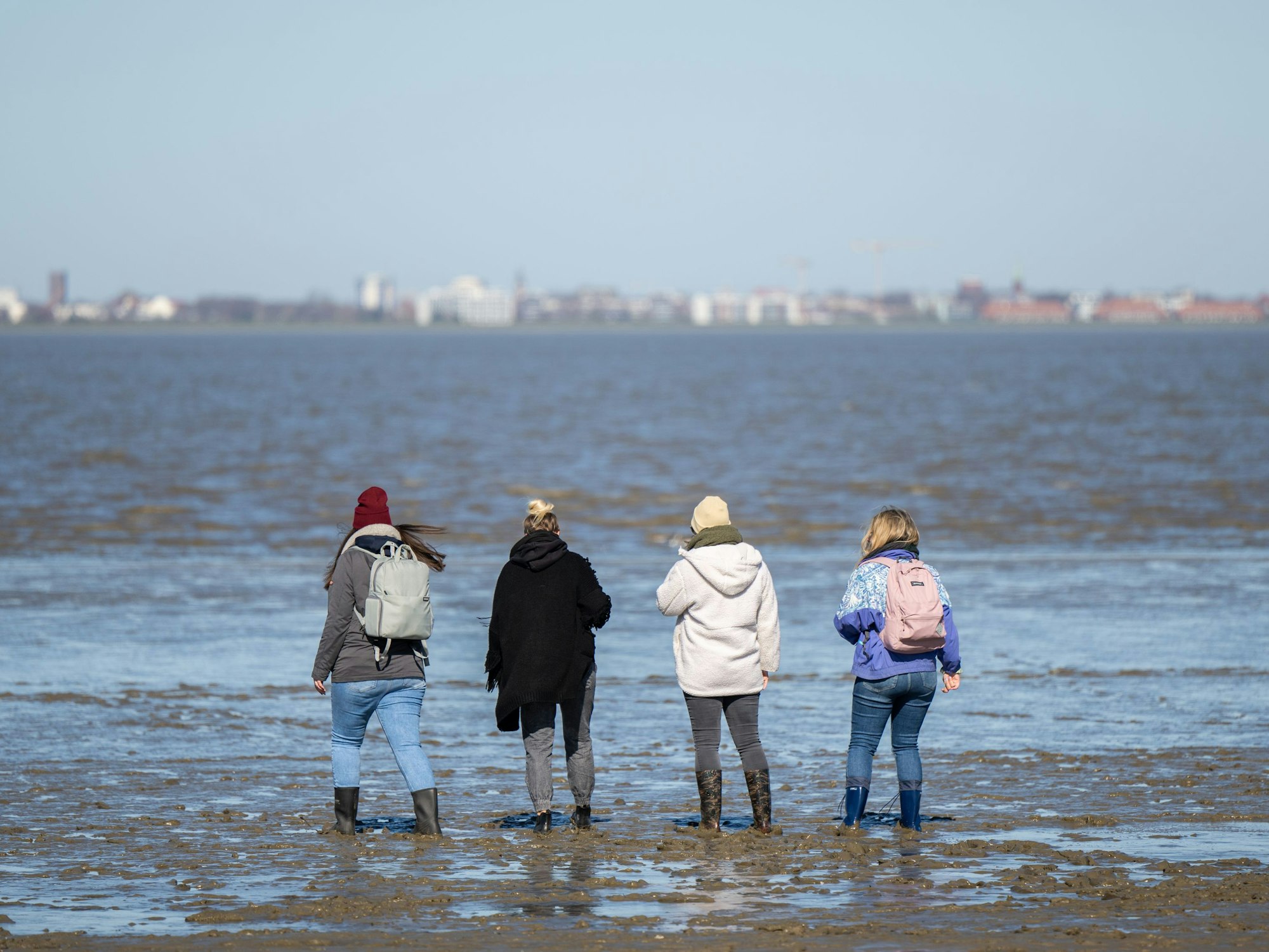 Vier Frauen sind bei Ebbe am Strand im Watt unterwegs, hier im März 2022 bei Dangast.