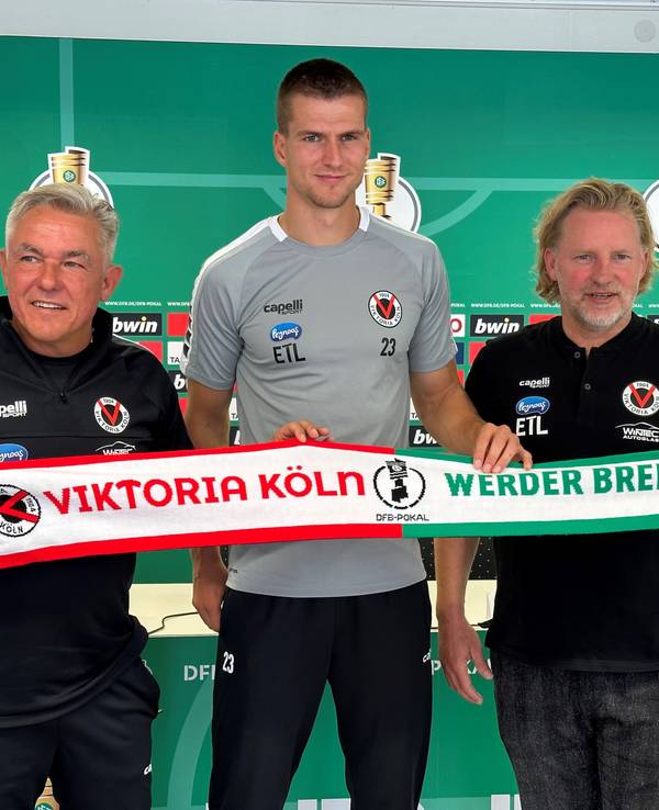 Viktoria-Trainer Olaf Janßen, Kapitän Moritz Fritz und Sportdirektor Stephan Küsters halten den Spieltagsschal in die Kamera.