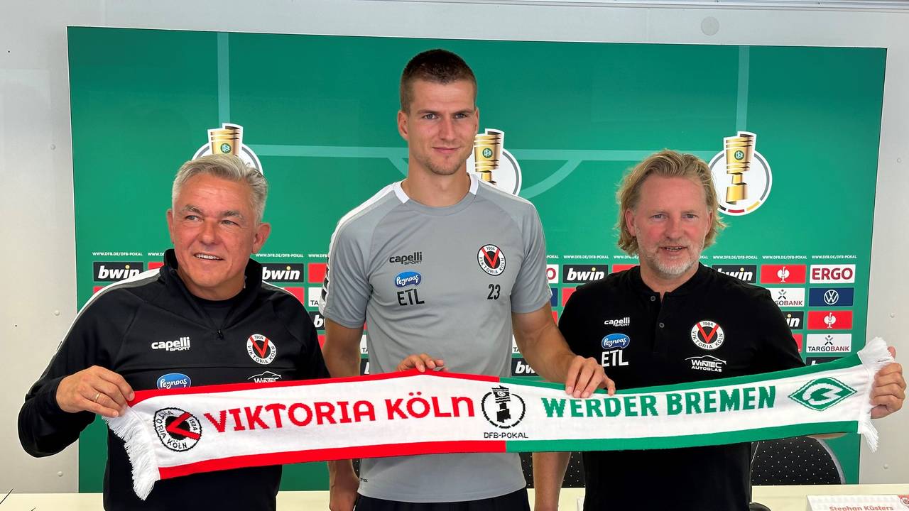 Viktoria-Trainer Olaf Janßen, Kapitän Moritz Fritz und Sportdirektor Stephan Küsters halten den Spieltagsschal in die Kamera.