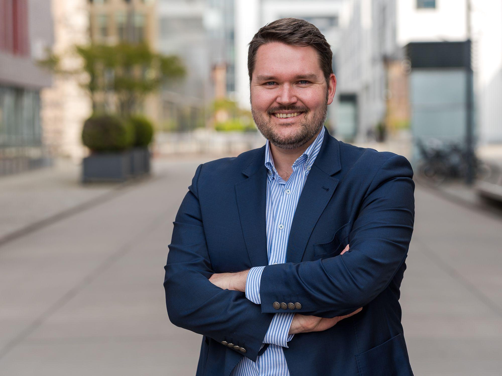 Philipp Hoffmann steht mit einem blauen Anzug und verschränkten Armen auf einer Straße in Köln.