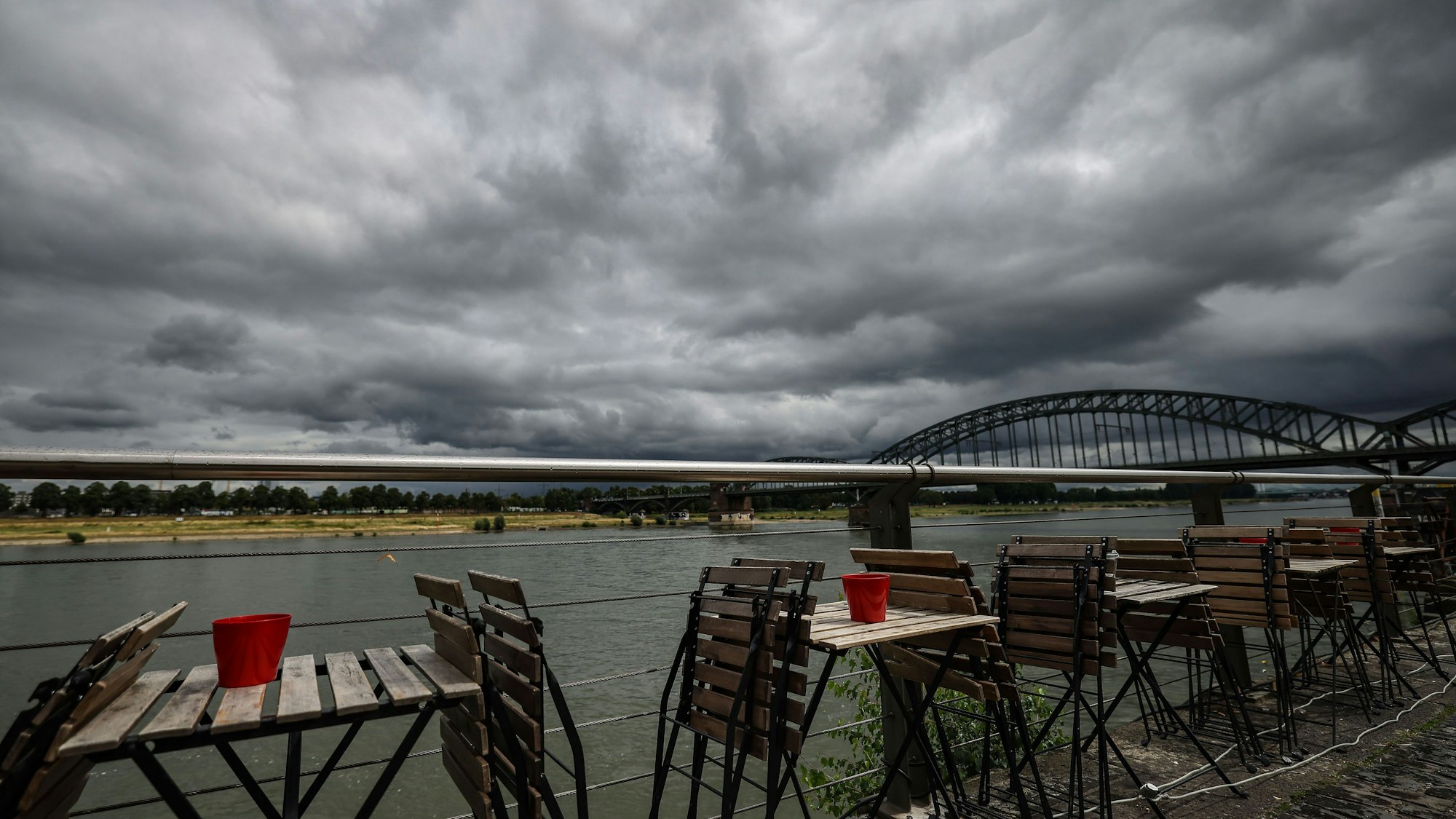 Stühle stehen Ende Juli vor einem Straßencafé am Rheinufer in Köln.