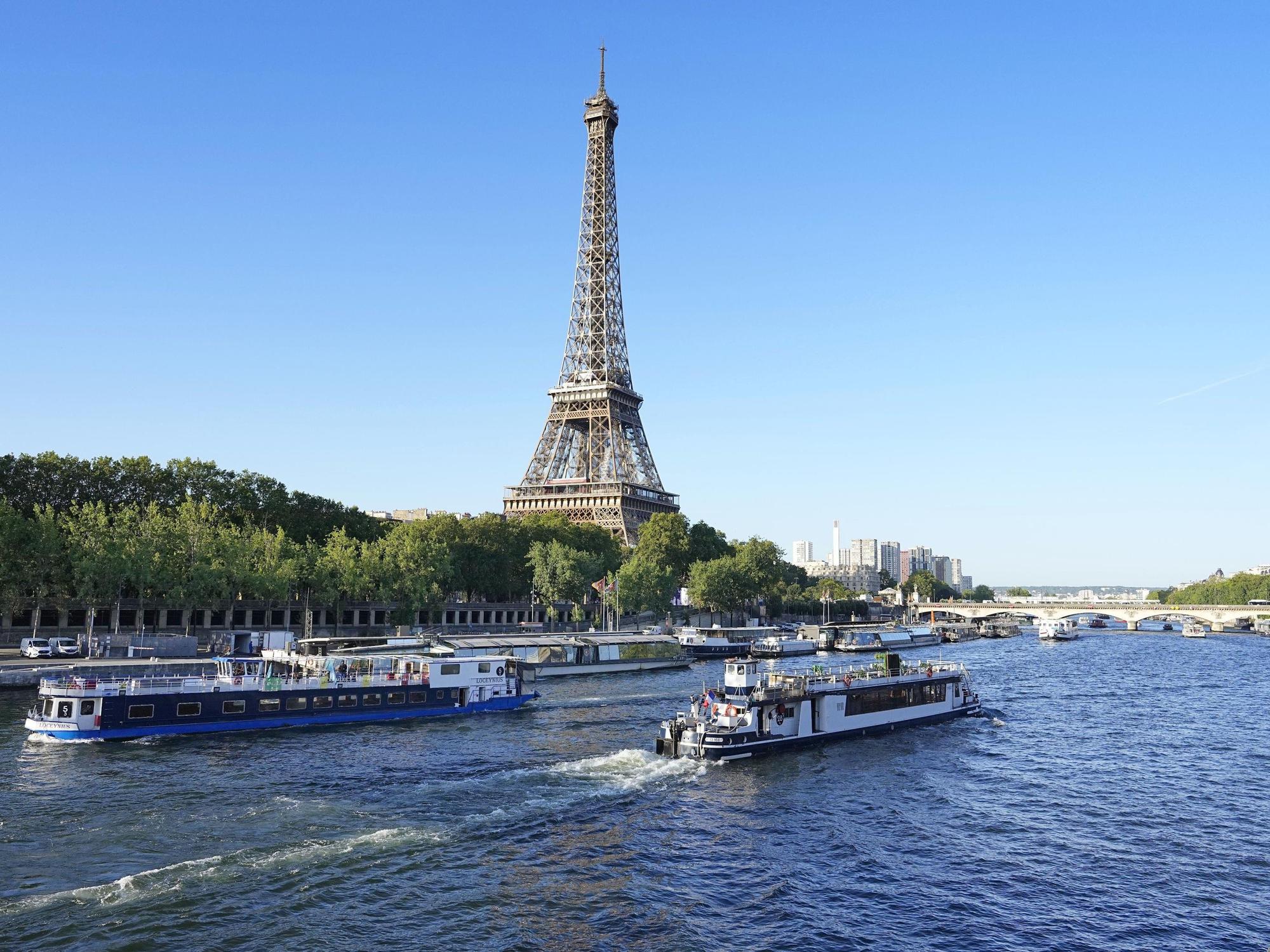Ein Boot und ein Lastkahn fahren am 17. Juli 2023 vor dem Eiffelturm auf der Seine in Paris.