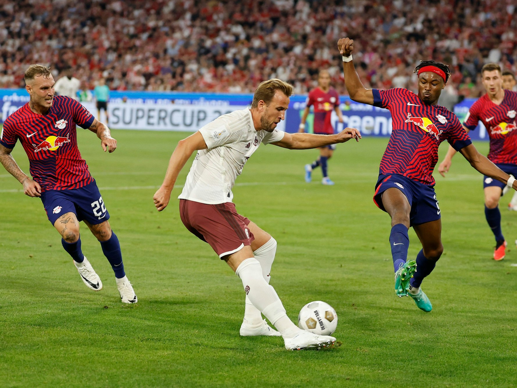 Bayerns Harry Kane (M) versucht sich gegen Leipzigs David Raum (l) und Leipzigs Mohamed Simakan durchzusetzen.