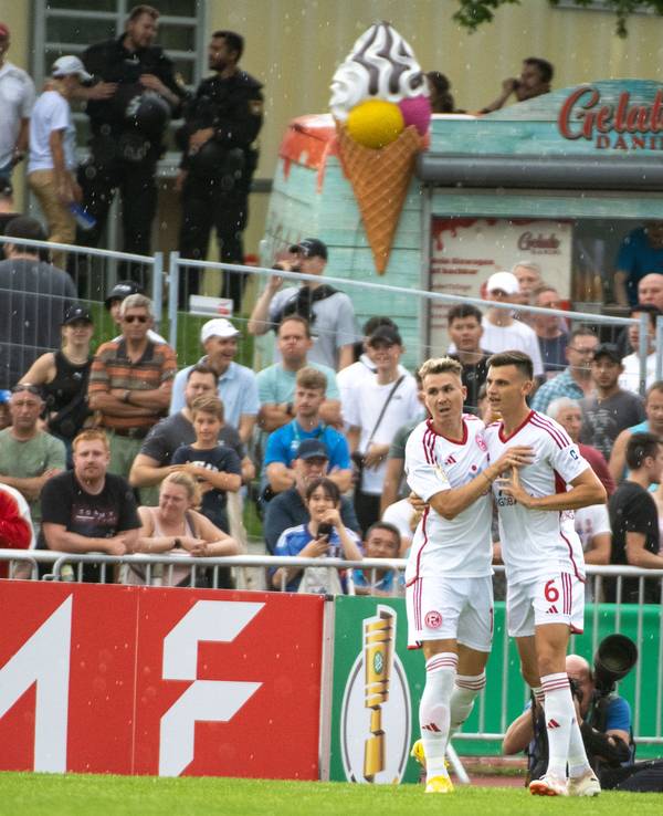 Düsseldorfs Felix Klaus (l) und Yannik Engelhardt jubeln nach dem 1:0. Im Hintergrund stehen ein paar wenige Zuschauerinnen und Zuschauer sowie ein Eiswagen.