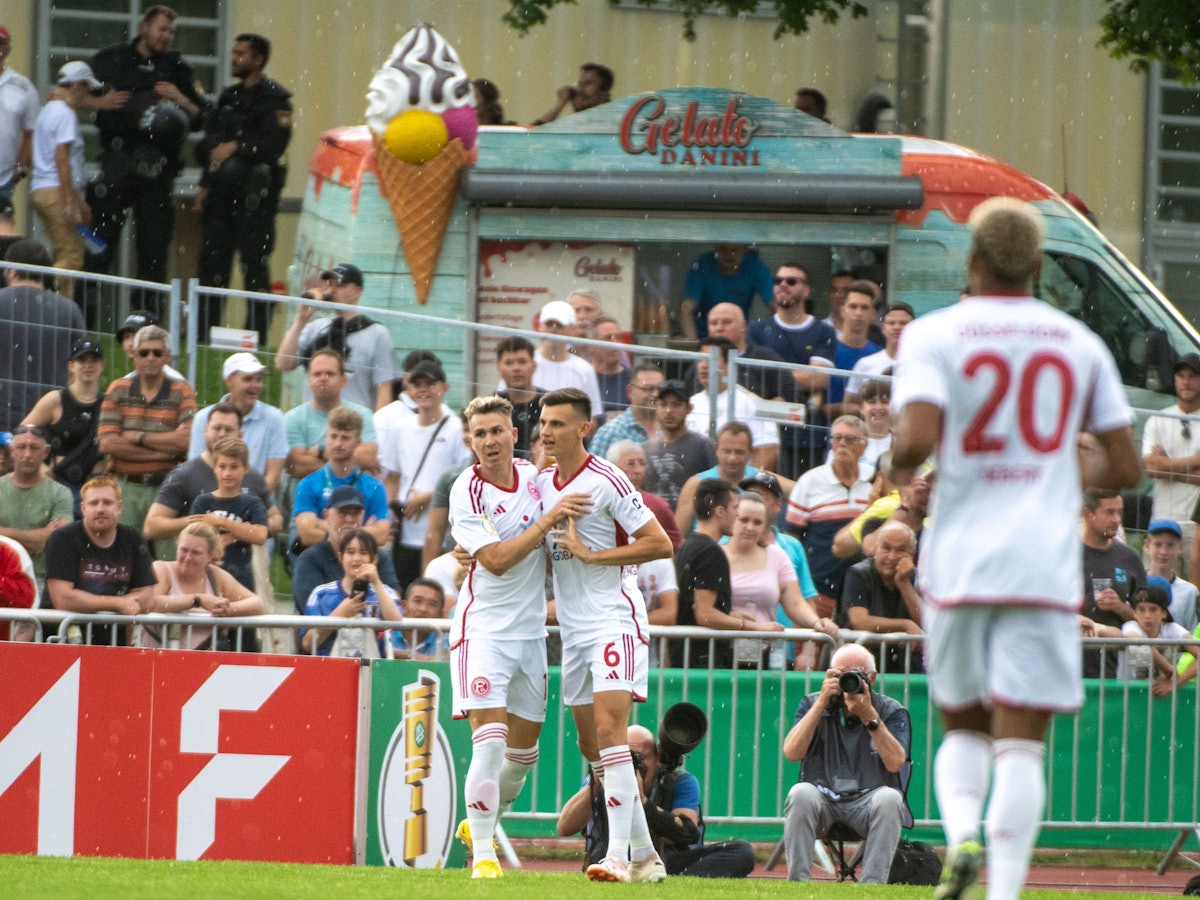 Düsseldorfs Felix Klaus (l) und Yannik Engelhardt jubeln nach dem 1:0. Im Hintergrund stehen ein paar wenige Zuschauerinnen und Zuschauer sowie ein Eiswagen.
