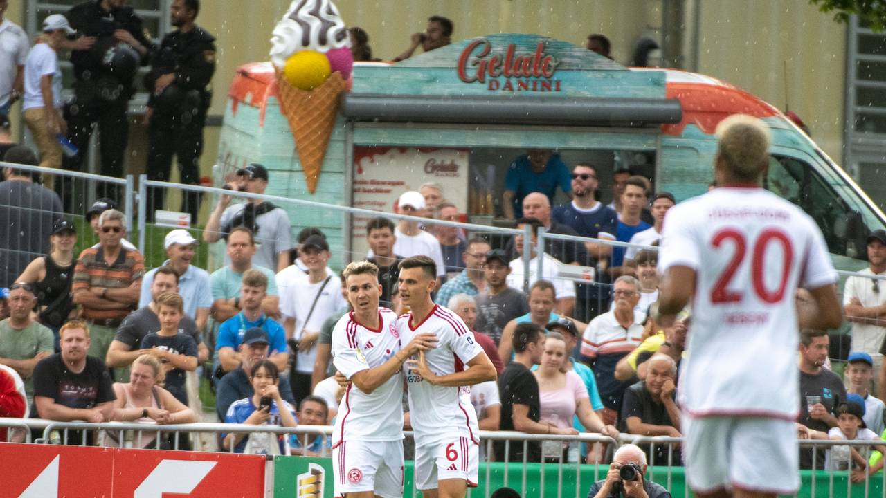 Düsseldorfs Felix Klaus (l) und Yannik Engelhardt jubeln nach dem 1:0. Im Hintergrund stehen ein paar wenige Zuschauerinnen und Zuschauer sowie ein Eiswagen.