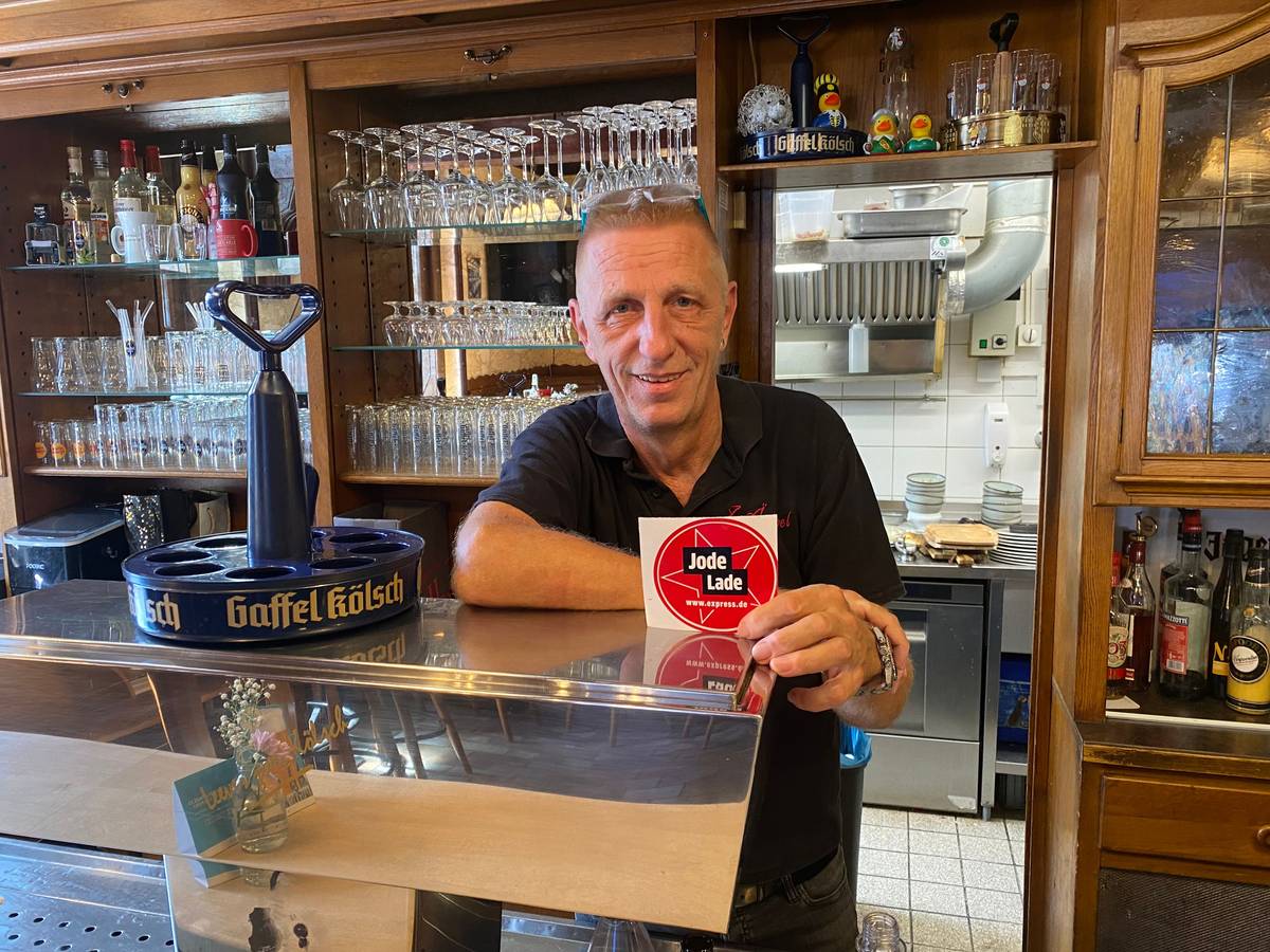 Ralf Klein steht hinter der Theke und zeigt die „Jode Lade“-Auszeichnung
