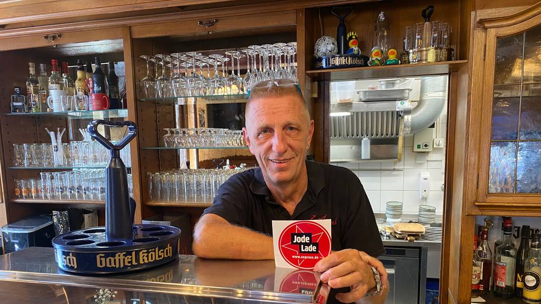 Ralf Klein steht hinter der Theke und zeigt die „Jode Lade“-Auszeichnung