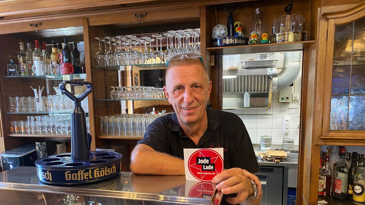 Ralf Klein steht hinter der Theke und zeigt die „Jode Lade“-Auszeichnung