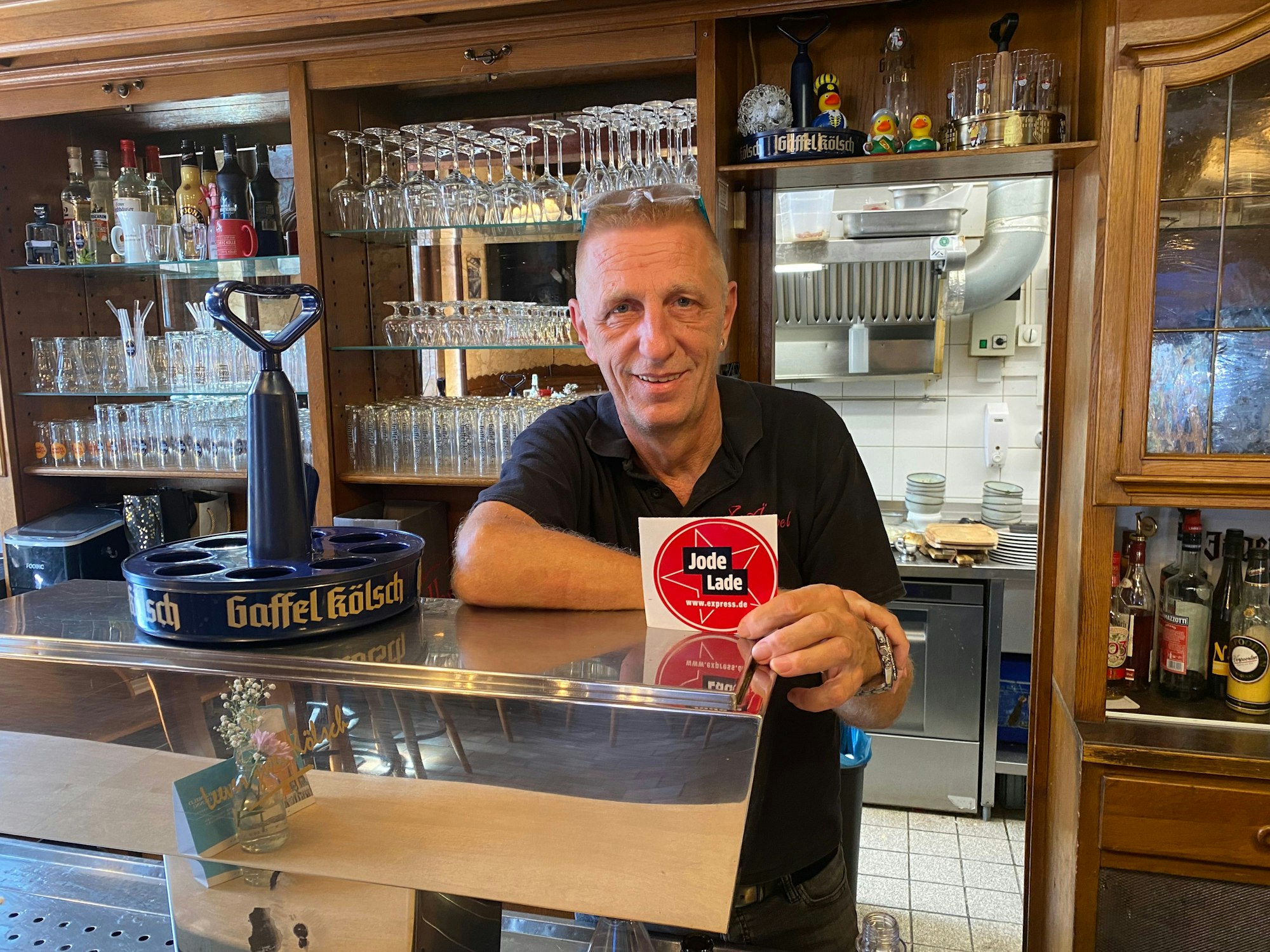 Ralf Klein steht hinter der Theke und zeigt die „Jode Lade“-Auszeichnung