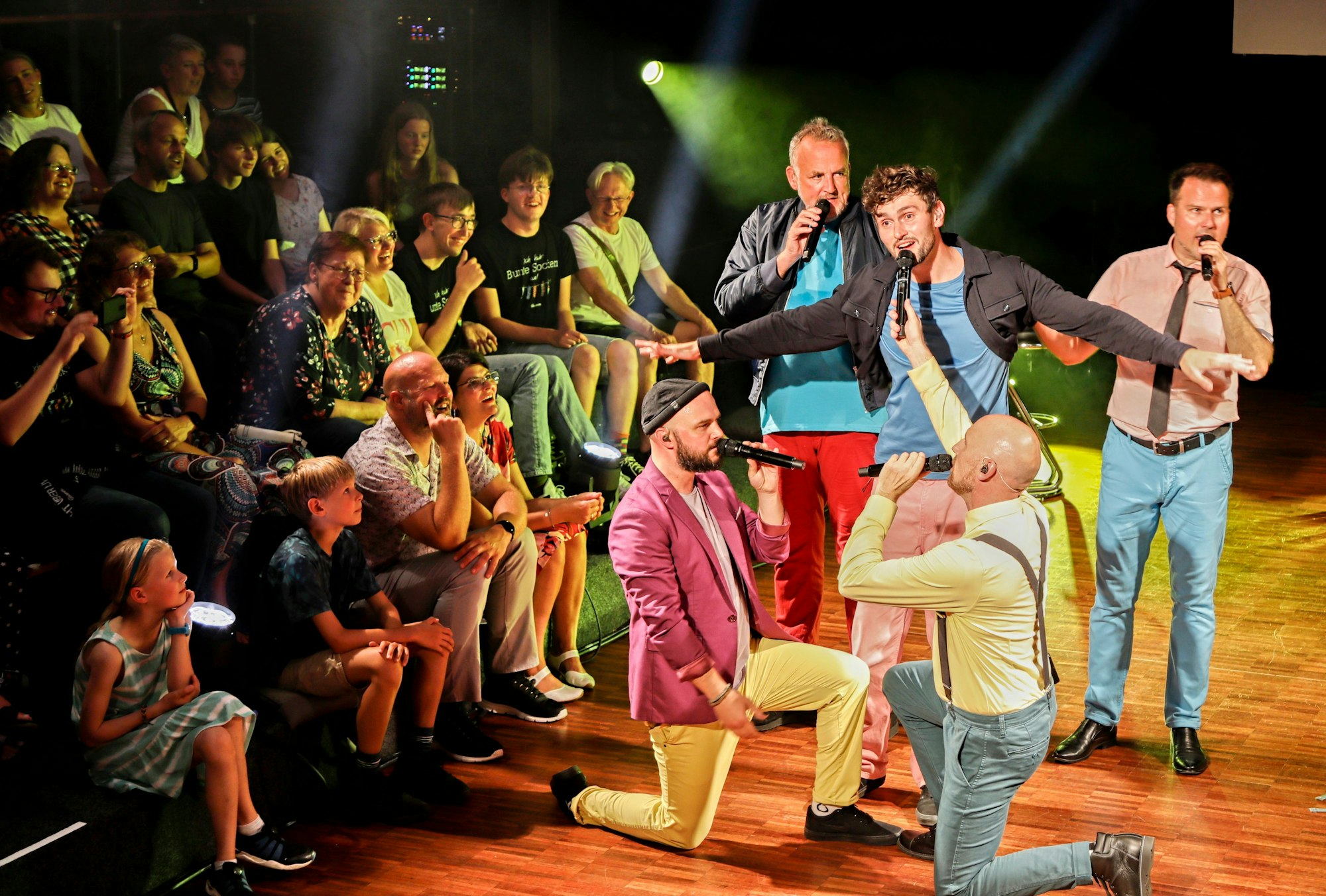 Die Mitglieder der Alten Bekannten singen in Mikros, das Publikum hört zu.