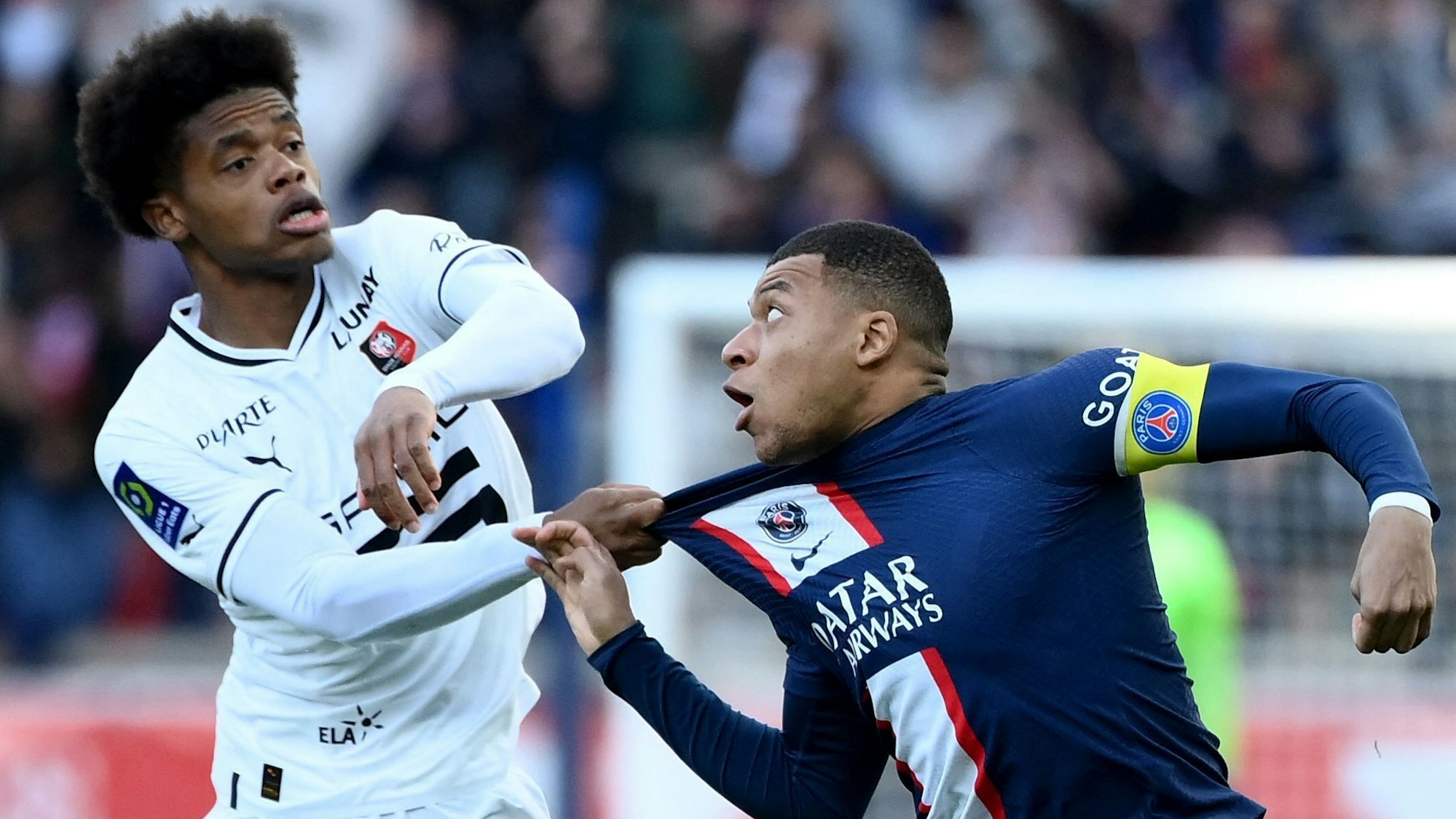 Warmed Omari zieht am Trikot von Kylian Mbappé, der Mund und Augen aufreißt.