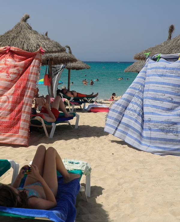 Menschen schützen sich bei hohen Temperaturen mit Strandtüchern vor der Sonne am Strand von Arenal.