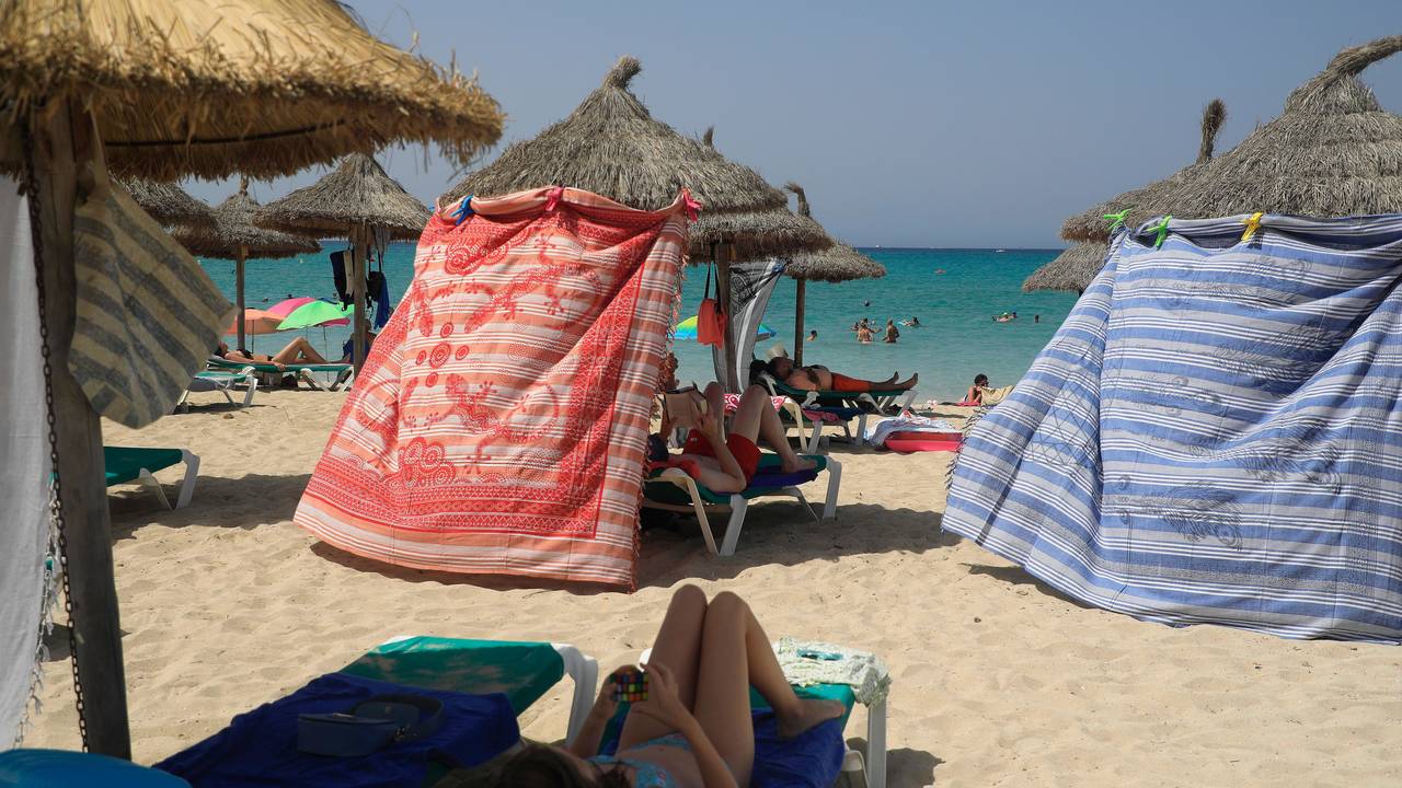 Menschen schützen sich bei hohen Temperaturen mit Strandtüchern vor der Sonne am Strand von Arenal.