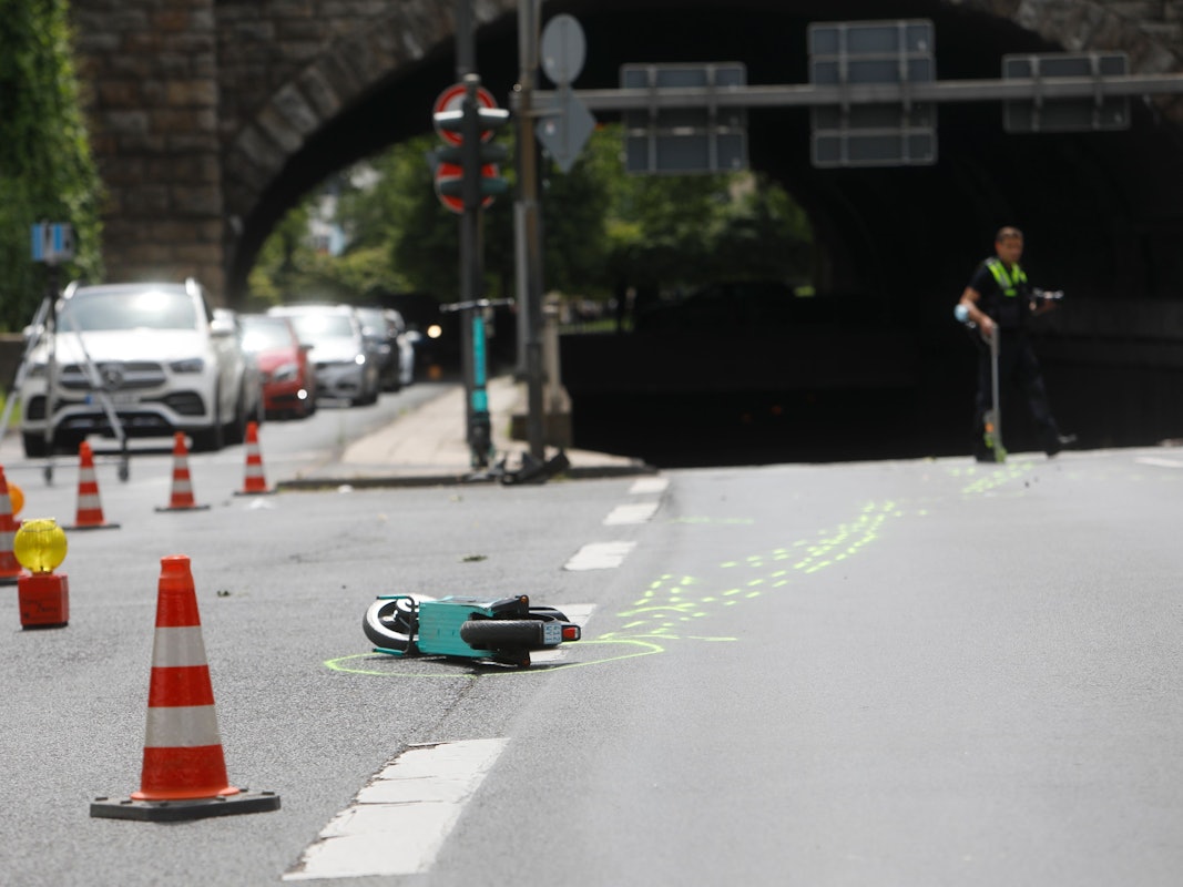 Ein kaputter E-Scooter liegt auf der Straße in Köln. Daneben sind Absperrungen der Polizei zu sehen.