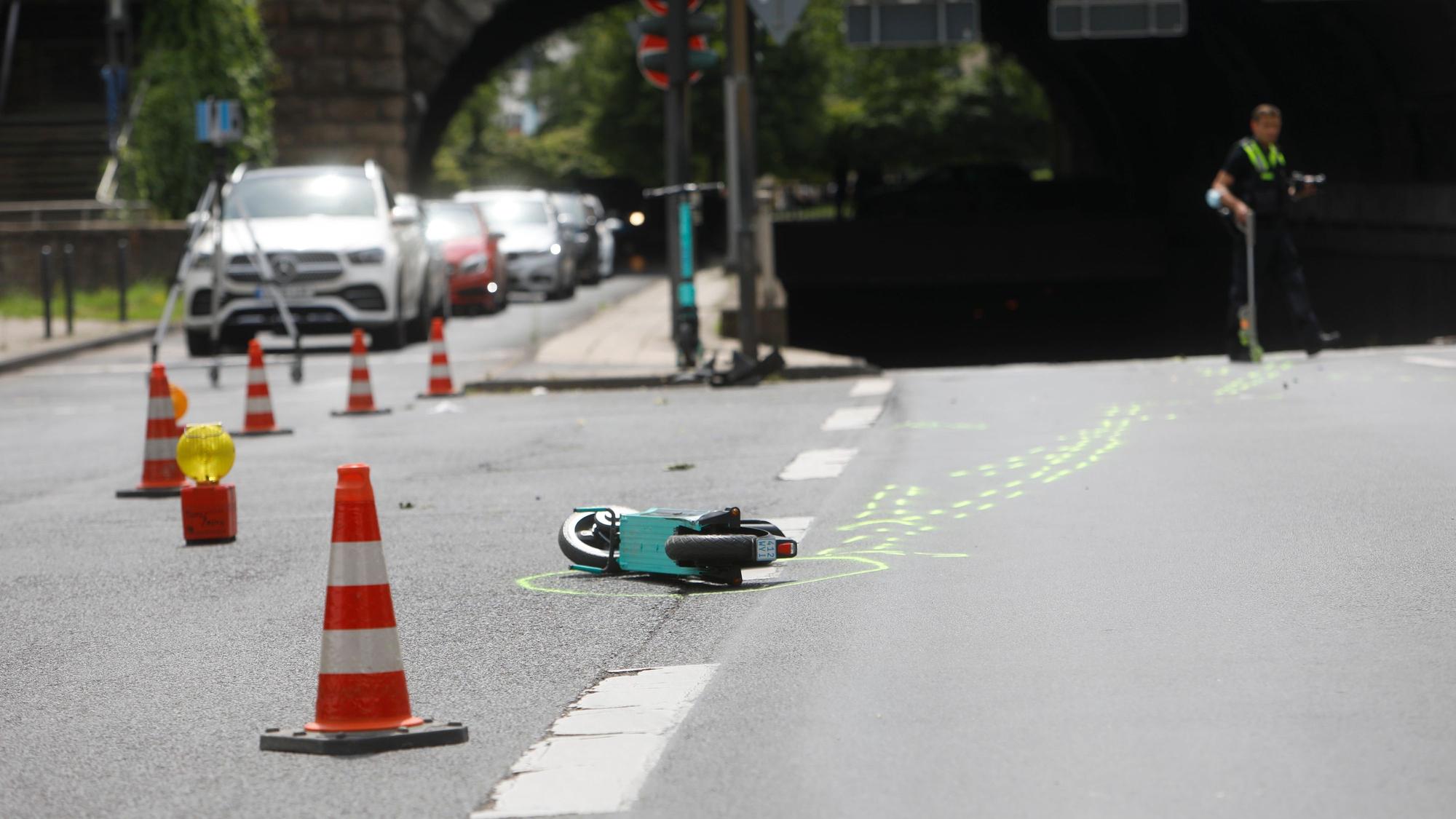 Ein kaputter E-Scooter liegt auf der Straße in Köln. Daneben sind Absperrungen der Polizei zu sehen.