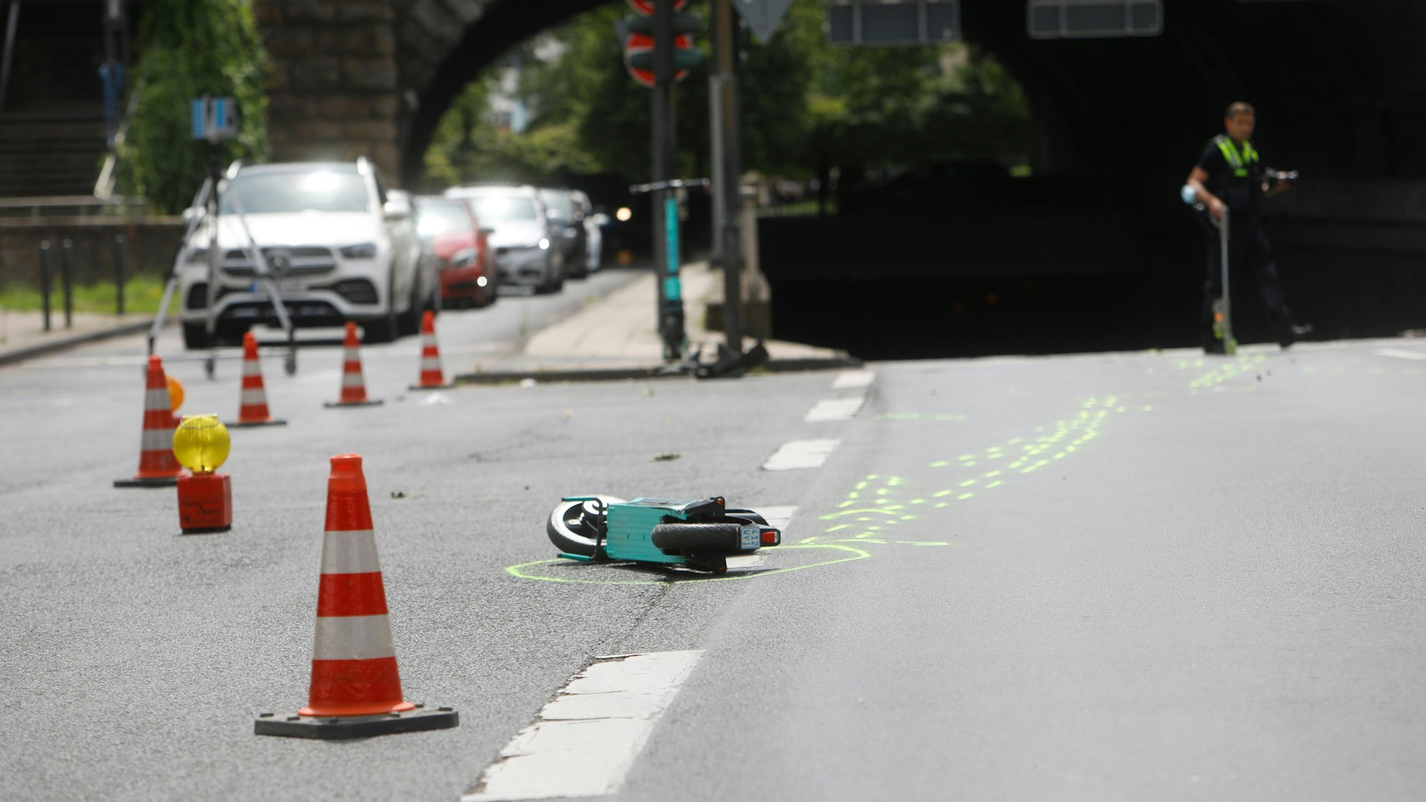 Ein kaputter E-Scooter liegt auf der Straße in Köln. Daneben sind Absperrungen der Polizei zu sehen.
