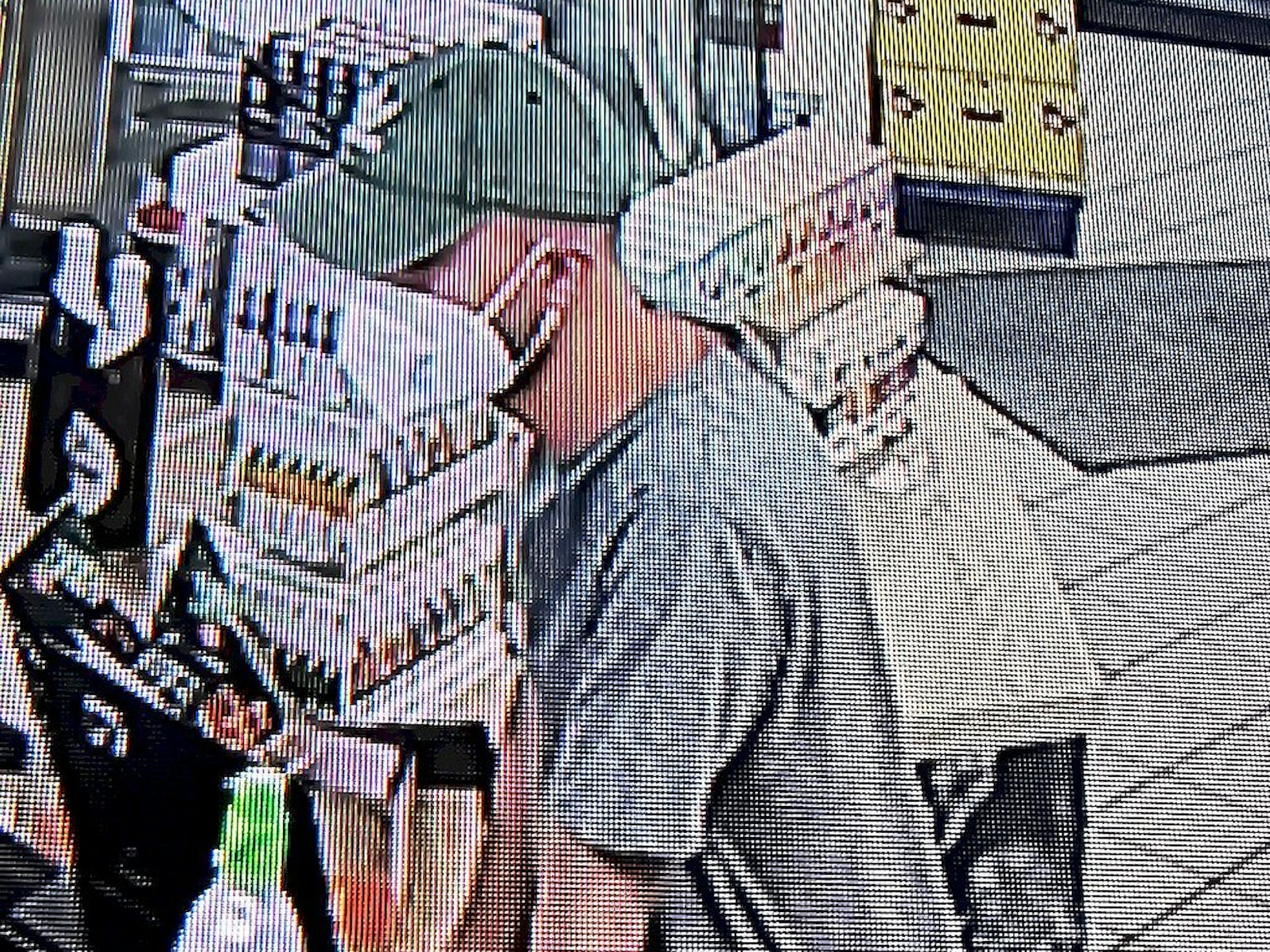 Ein Mann mit Gesichtsmaske und Kappe lehnt sich über den Schalter einer Tankstelle.