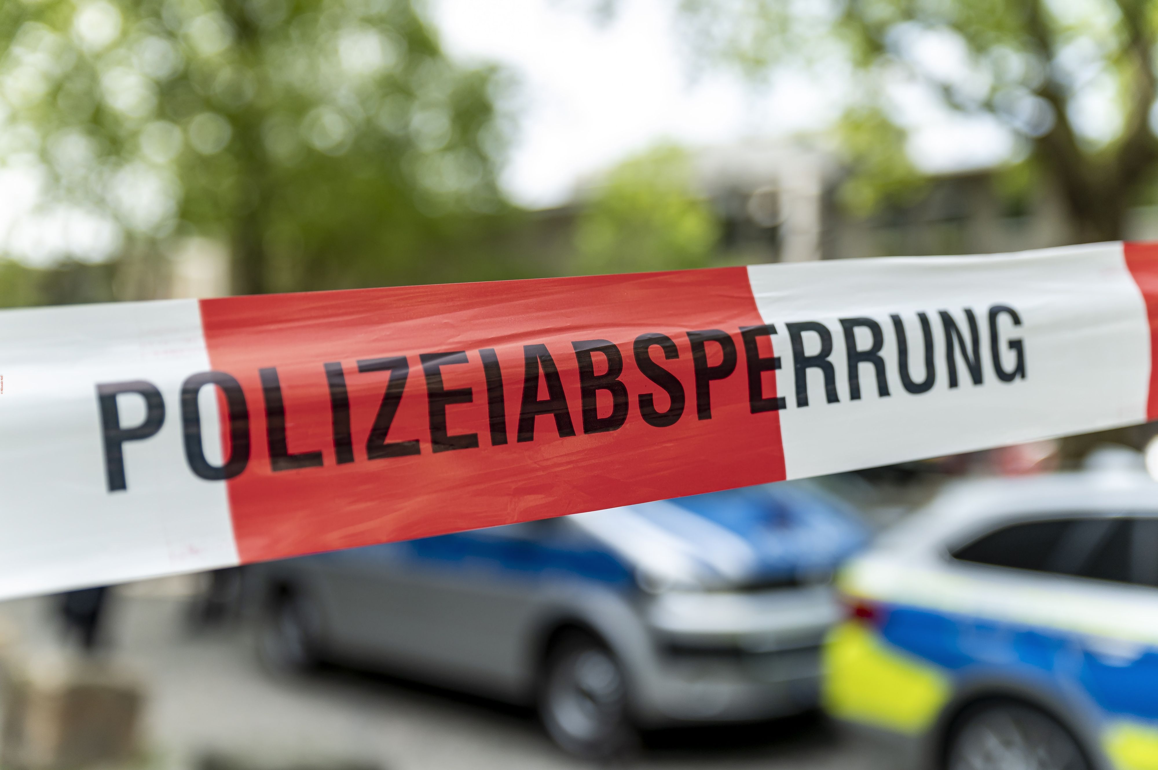 Polizei-Autos stehen an einem Tatort, im Vordergrund ist rot-weißes Absperrband zu sehen.