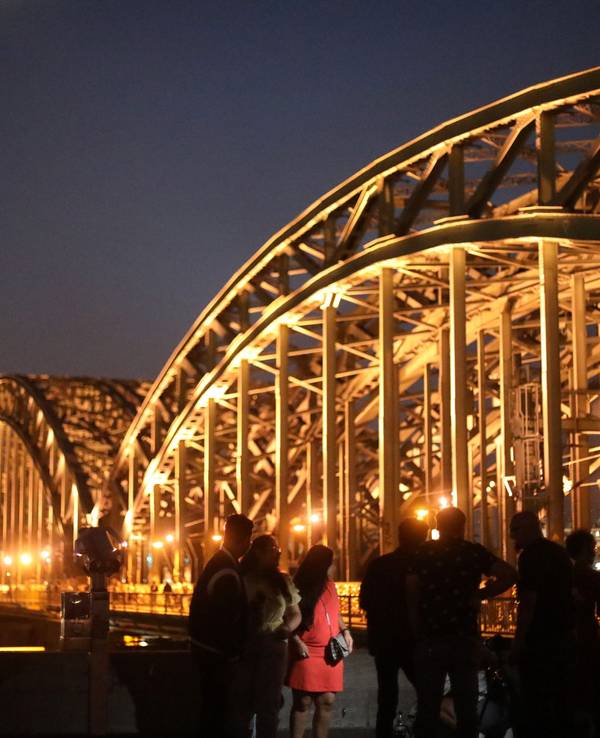 Menschen posieren vor dem Kölner Dom und der Hohenzollernbrücke am Rheinboulevard in Deutz