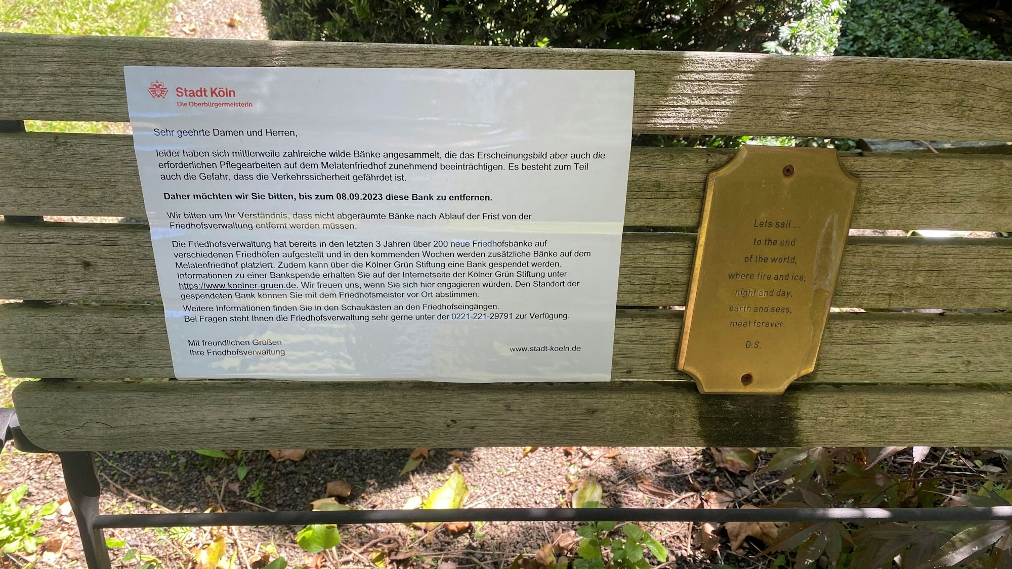 Eine Bank auf dem Melatenfriedhof. Auf ihr ist ein Hinweisschild der Stadt Köln angebracht, dass sie entfernt werden soll.