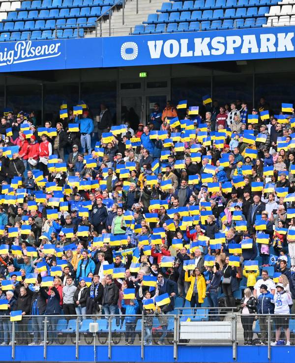 Die Zuschauer des Benefizspiels am 28. Mai 2022 stehen auf ihren Plätzen und halten Plakate mit der ukrainischen Fahne in die Höhe, während die ukrainische Nationalhymne gespielt wird.