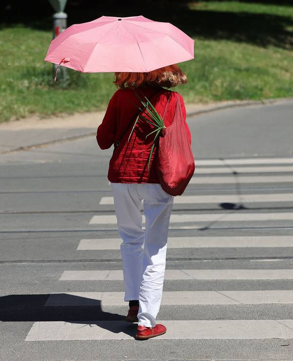 Eine Frau geht mit einem Regenschirm als Sonnenschirm durch Bonn: In Teilen von NRW warnt der Wetterdienst am Samstag vor Hitze.