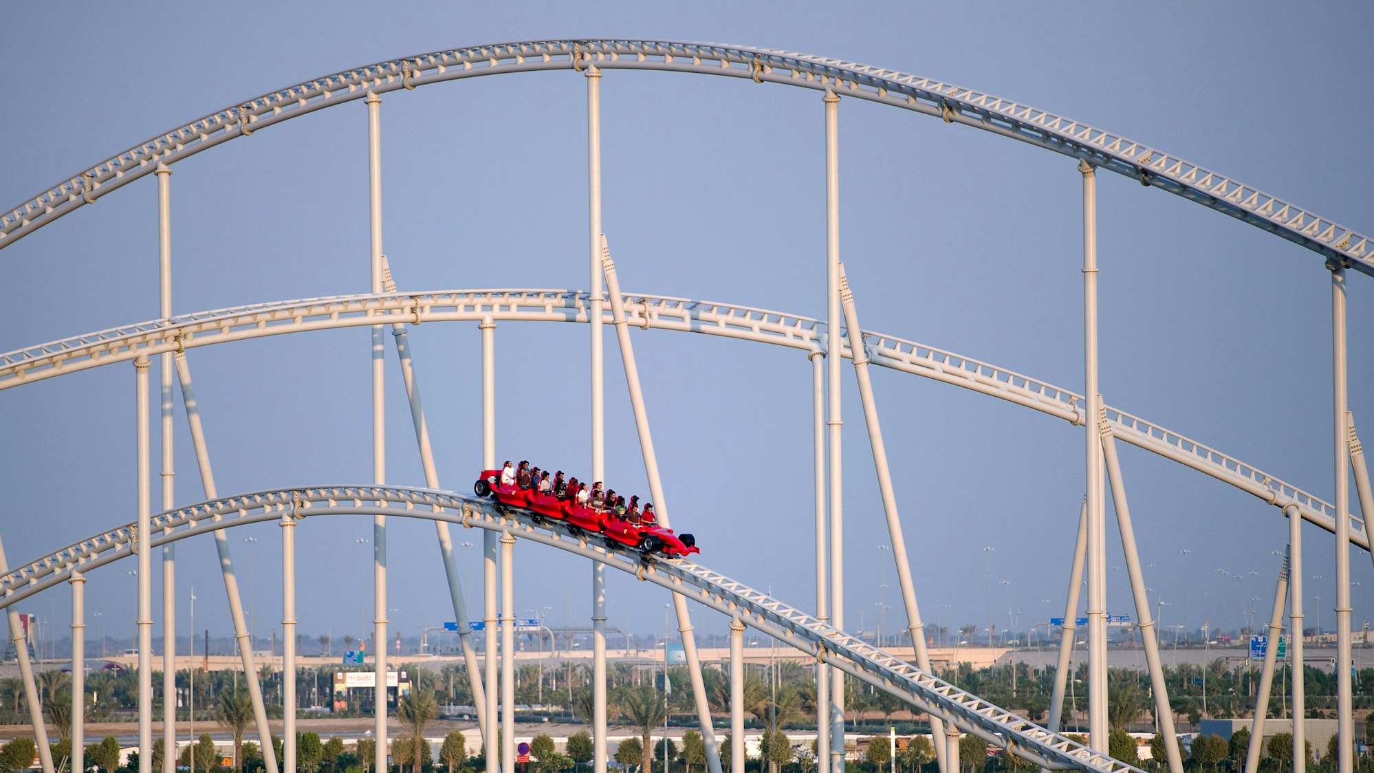 Eine Bahn der Achterbahn in der Ferrari World ist unterwegs, im Hintergrund sind Teile der Stadt Abu Dhabi zu sehen.