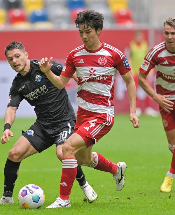 Ao Tanaka führt den Ball im Spiel gegen den SC Paderborn, er wird verfolgt von Florent Muslija.