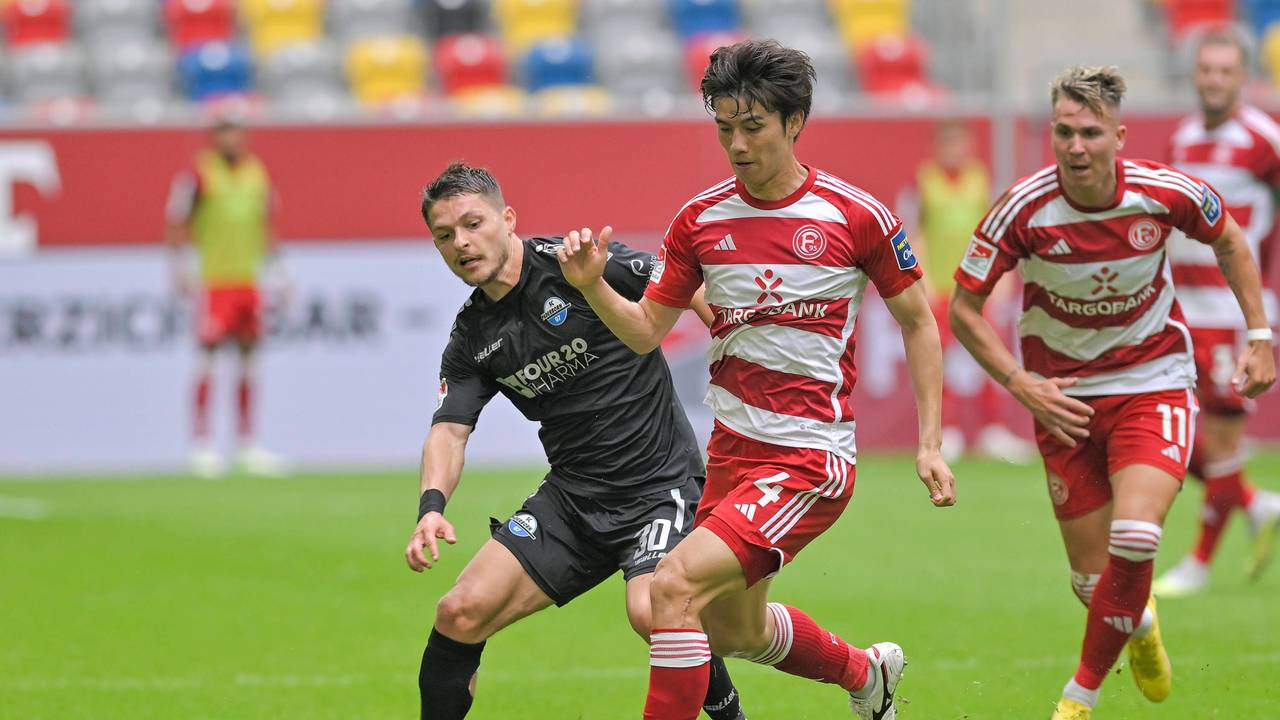 Ao Tanaka führt den Ball im Spiel gegen den SC Paderborn, er wird verfolgt von Florent Muslija.