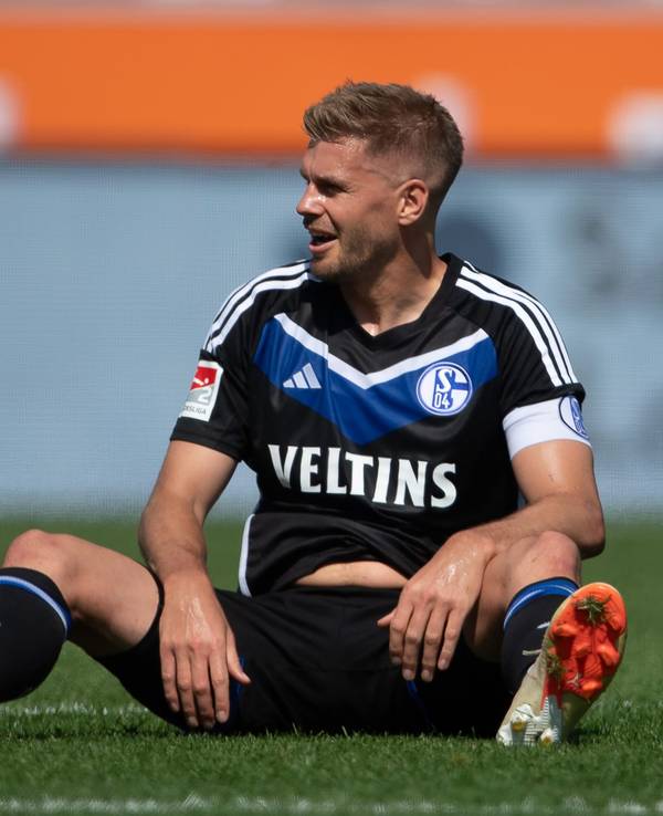 Simon Terodde sitzt im Schalke-Trikot auf dem Rasen.