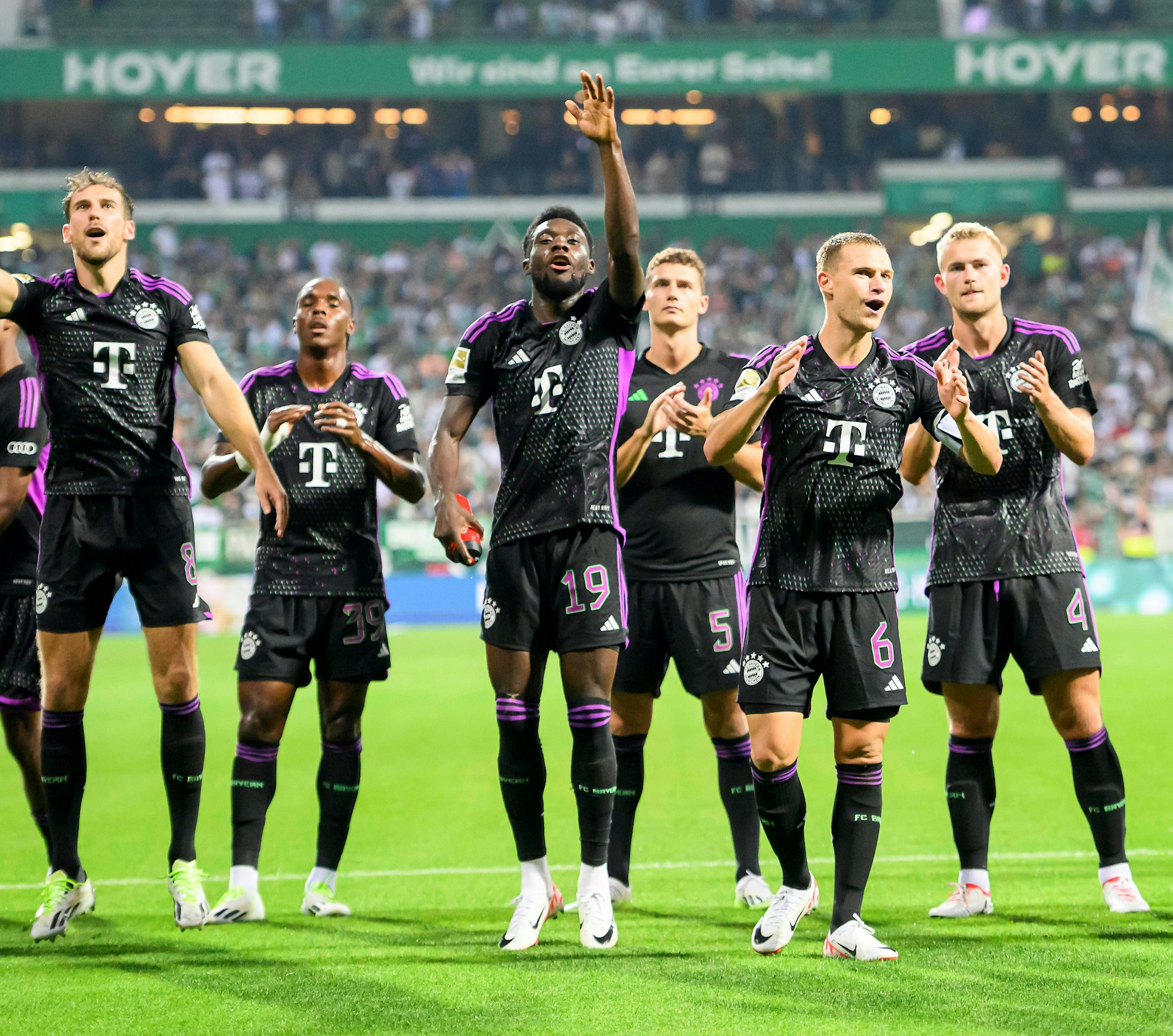 Leon Goretzka, Mathys Tel, Alphonso Davies, Benjamin Pavard, Joshua Kimmich und Matthjis de Ligt stehen vor dem Bayern-Block in Bremen.