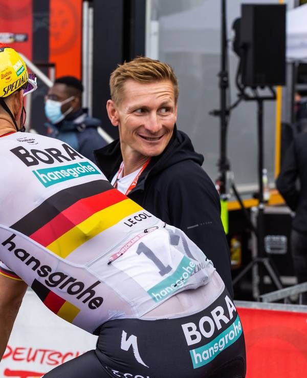 Nils Politt vom Team Bora-Hansgrohe (vorne) im Zielbereich mit dem ehemaligen Radprofi Andre Greipel.