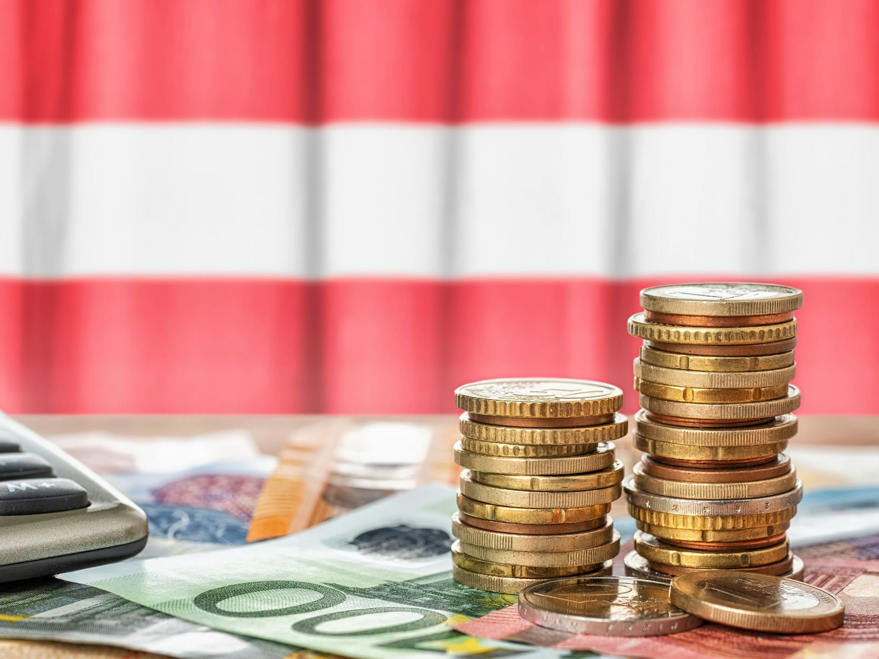 Euromünzen vor einer Österreichflagge.