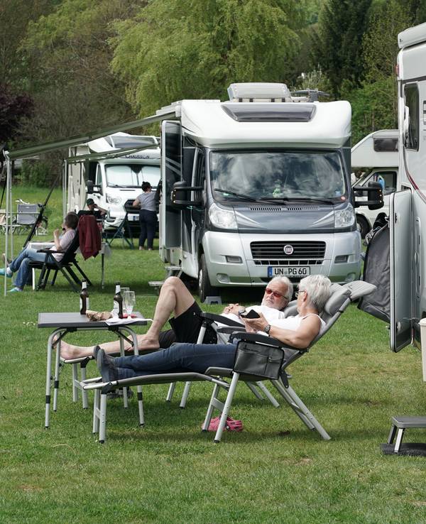 Urlauber und Urlauberinnen entspannen vor ihrem Wohnmobil.