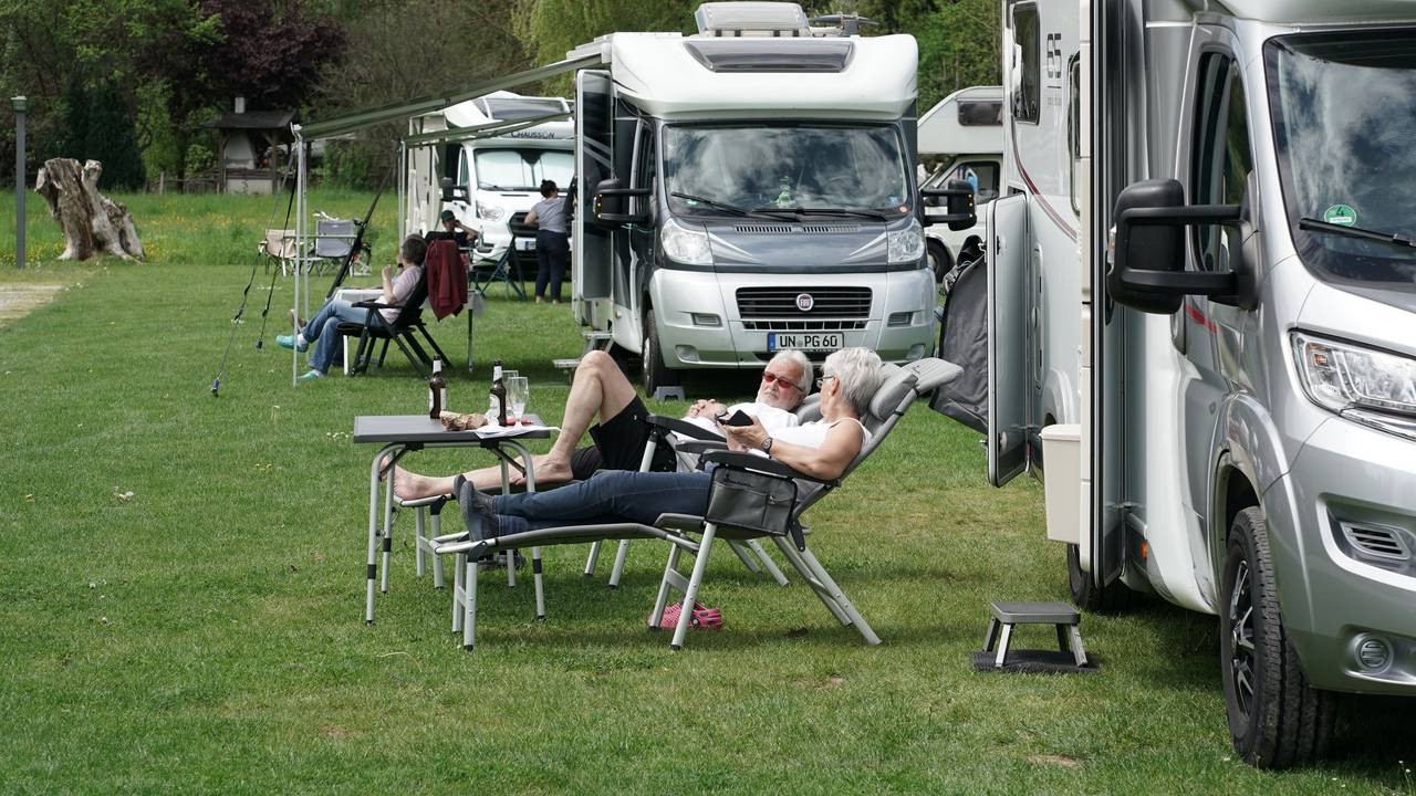 Urlauber und Urlauberinnen entspannen vor ihrem Wohnmobil.