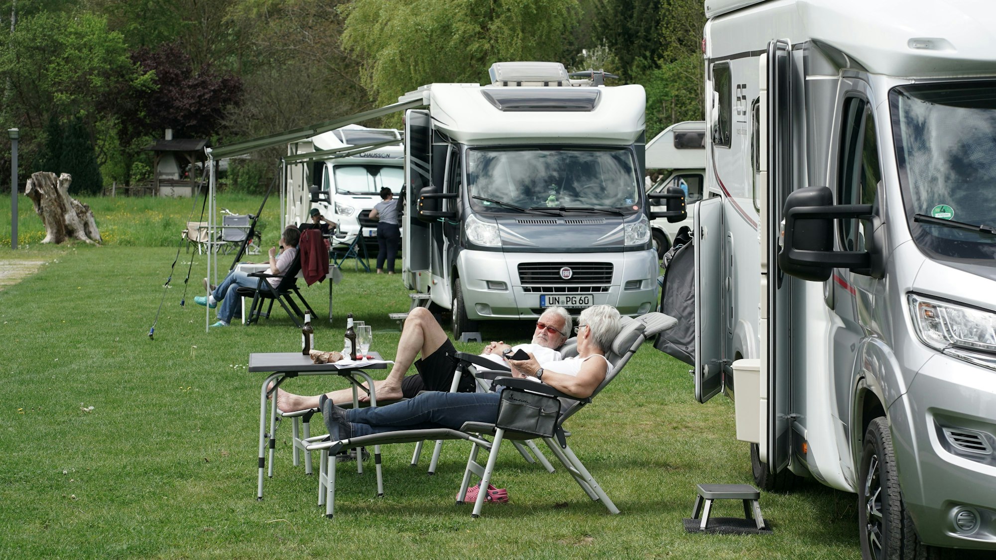 Urlauber und Urlauberinnen entspannen vor ihrem Wohnmobil.