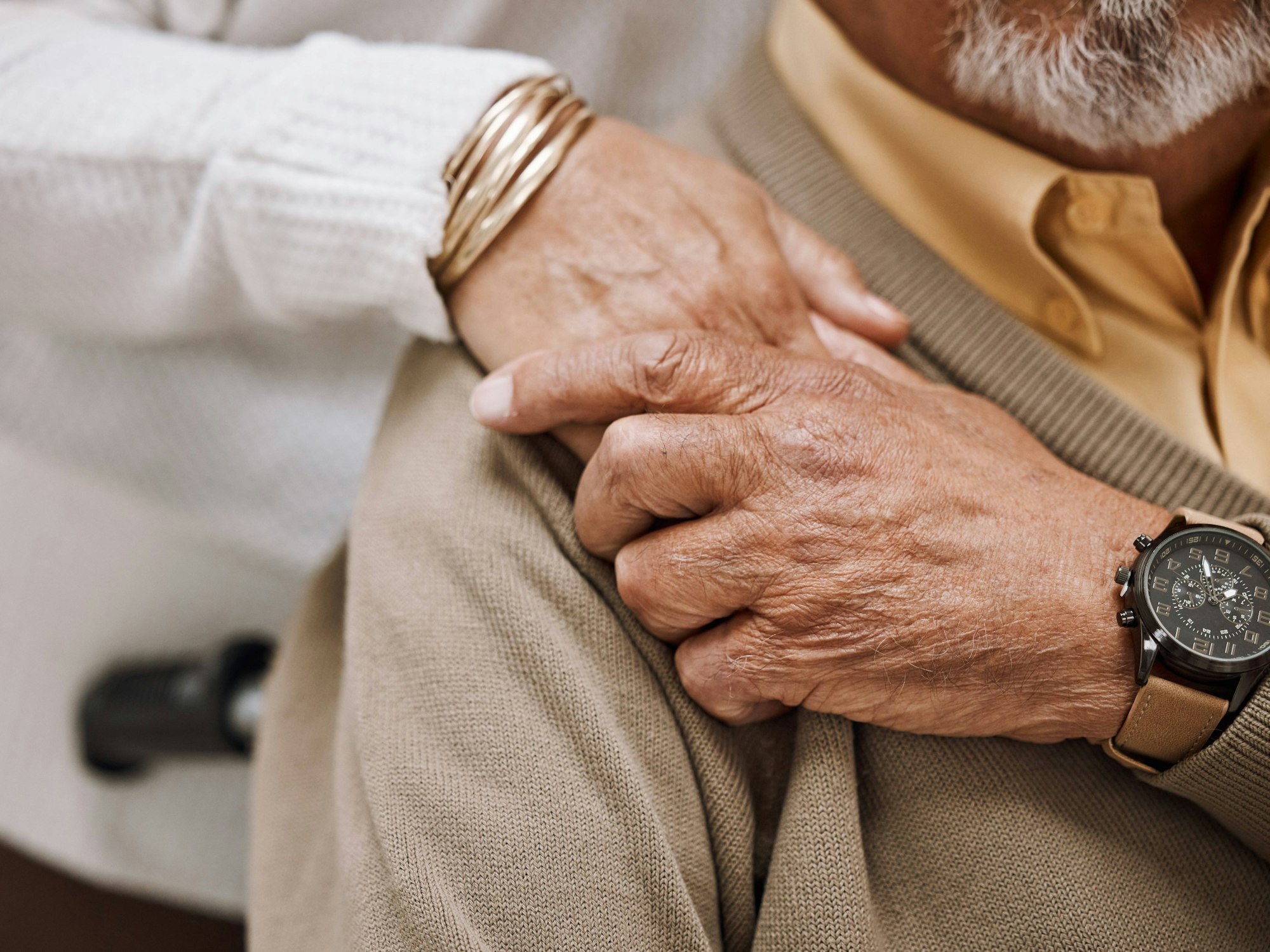 Die Hand eines älteren Mannes berührt die Hand einer älteren Frau, welche auf der Schulter des Mannes ruht.