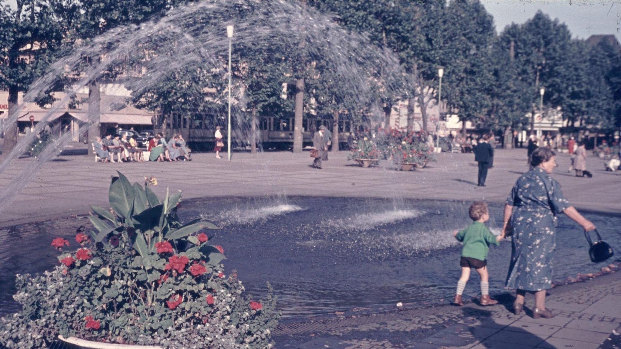 Der ehemalige Brunnen am Neumarkt. Im Vordergrund nimmt eine Frau ihr Kind an die Hand.