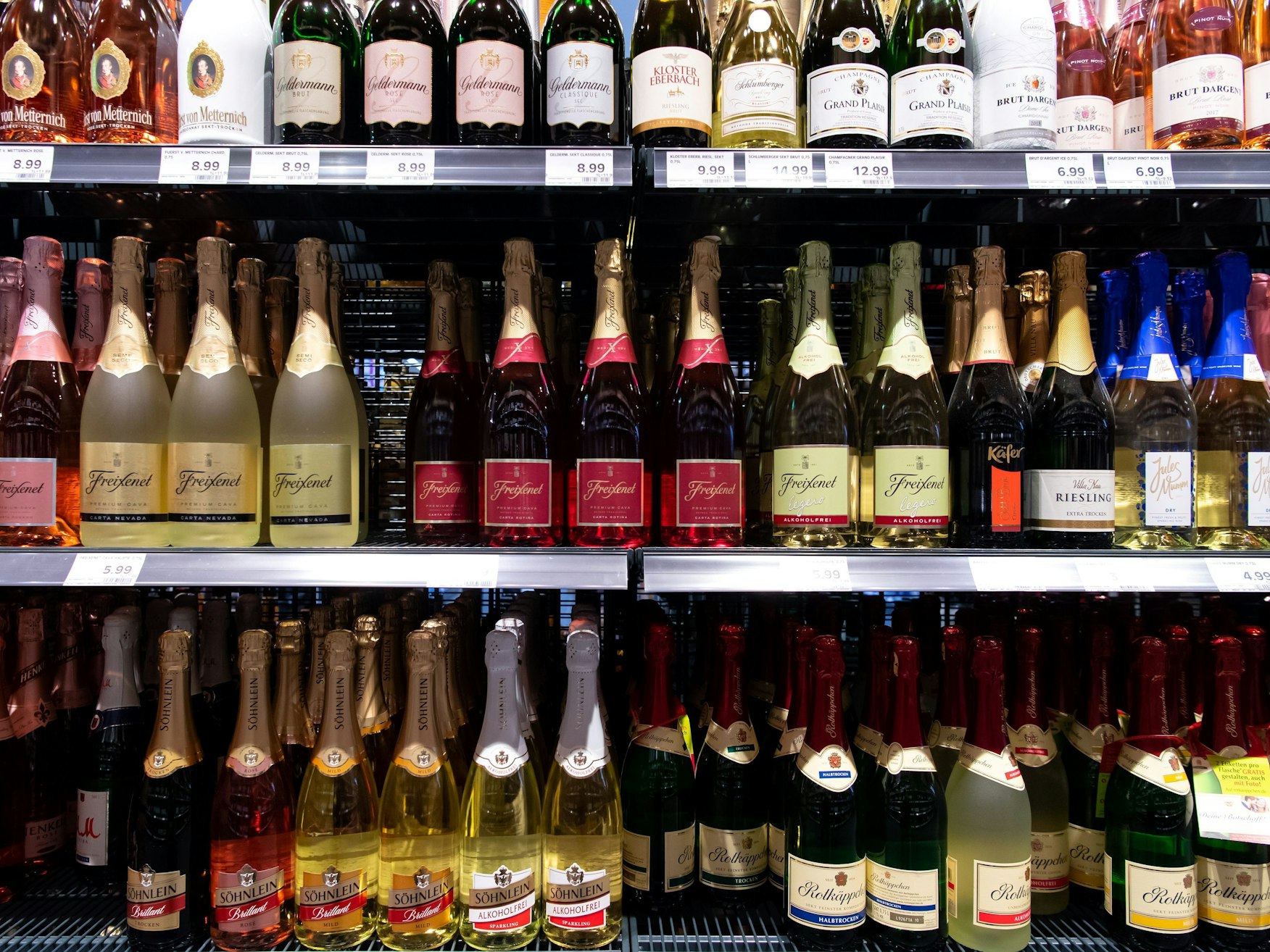 Sektflaschen von verschiedenen Herstellern stehen in einem Supermarktregal.