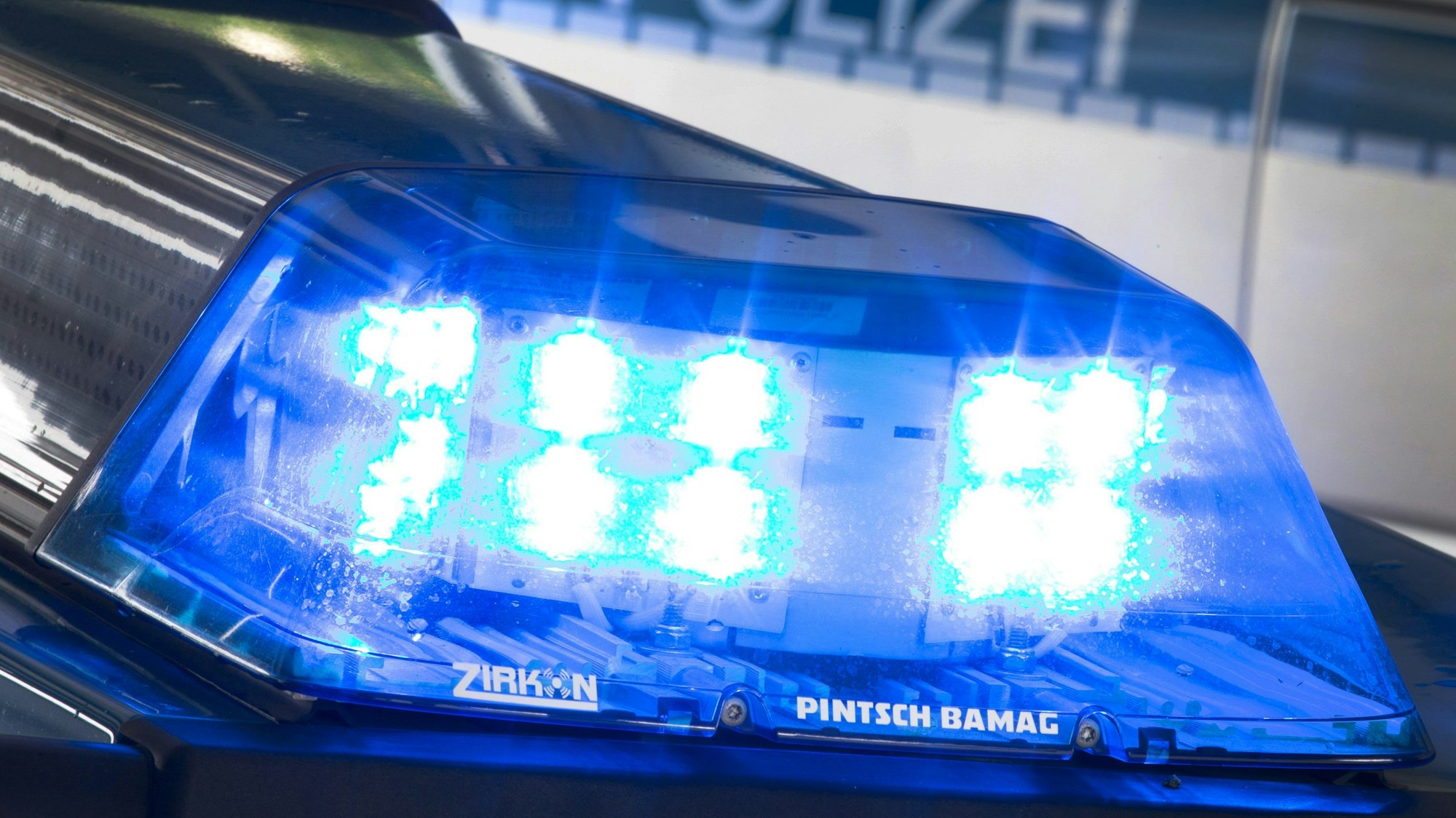 Ein Blaulicht leuchtet auf dem Dach eines Polizeiwagens. Im Hintergrund steht ein weiterer Streifenwagen.