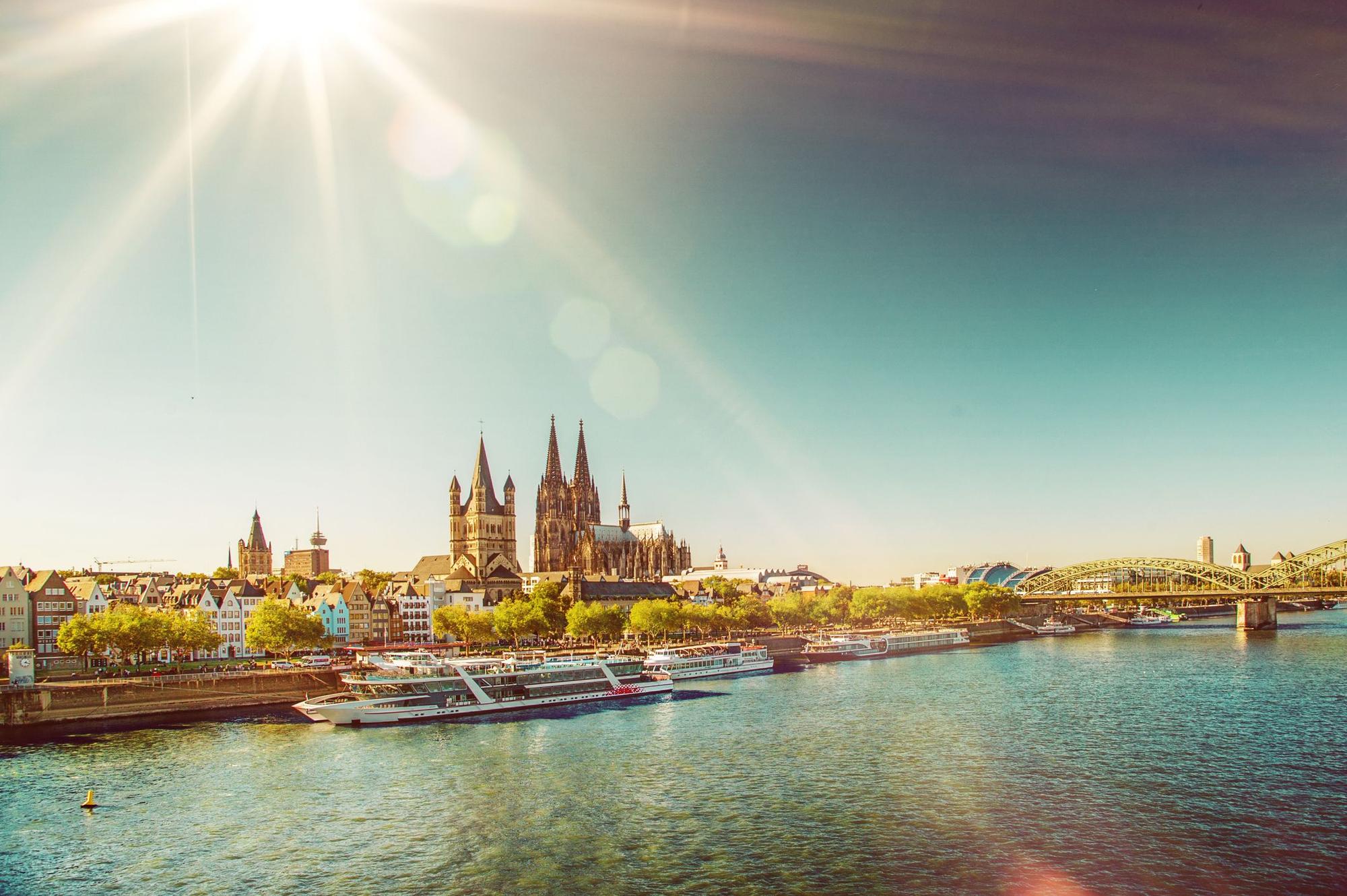 View on the old town of Cologne and Cologne Cathedral with Hohenzollern Bridge and several white passenger boats on the river Rhine on a sunny day in summer