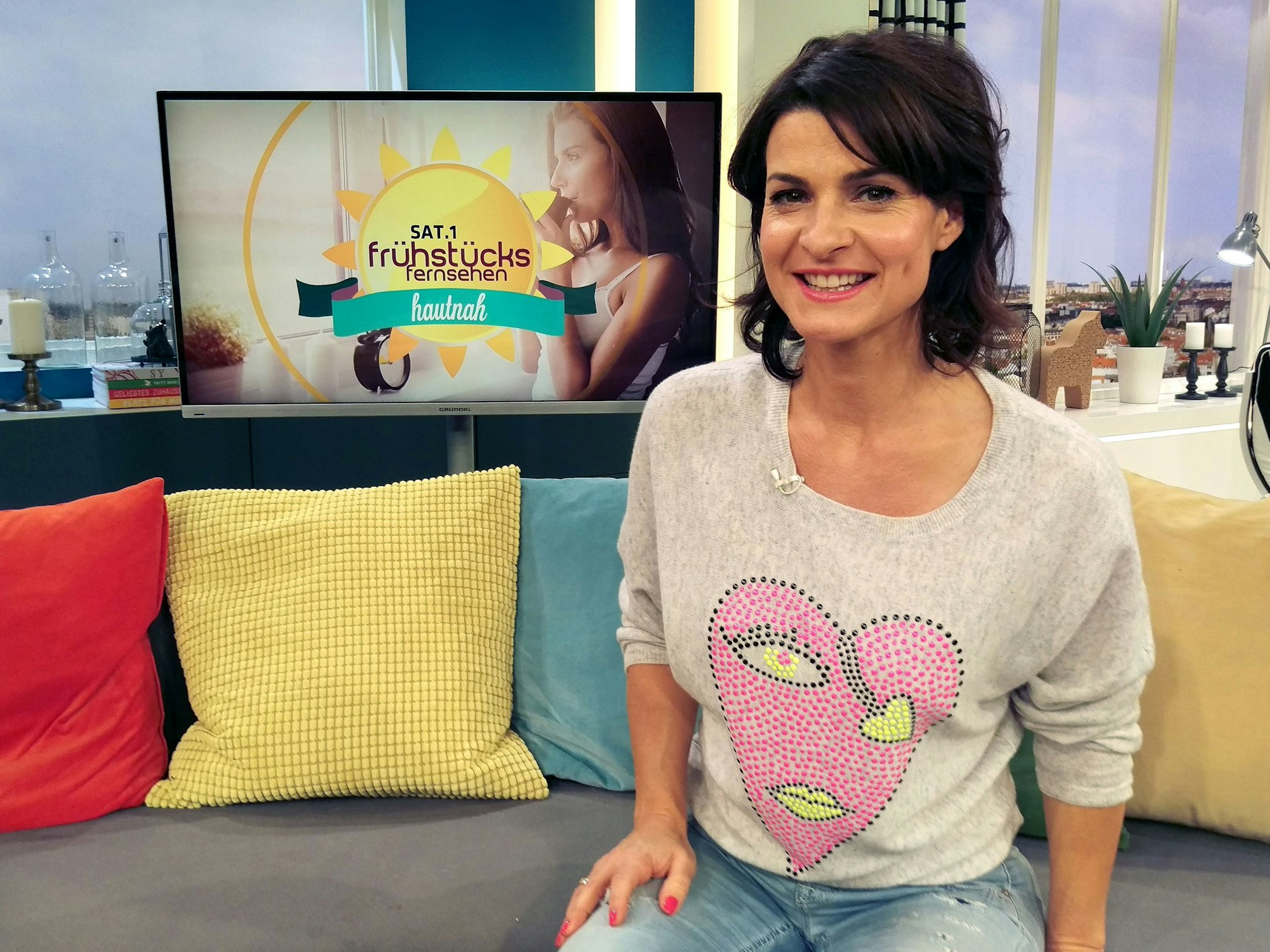 Marlene Lufen, Moderatorin des Sat.1-Frühstückfernsehens, trägt einen grauen Pullover mit einem großen, rosafarbenen Herz.