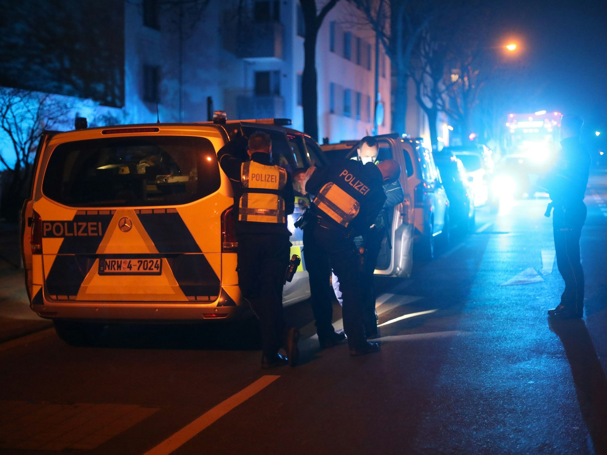 Polizei steht in der Nacht an einer Straße und durchsucht einen Autofahrer.
