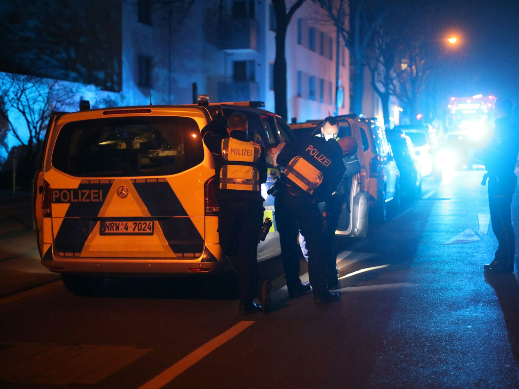 Polizeibeamte stehen nachts an einem Streifenwagen.